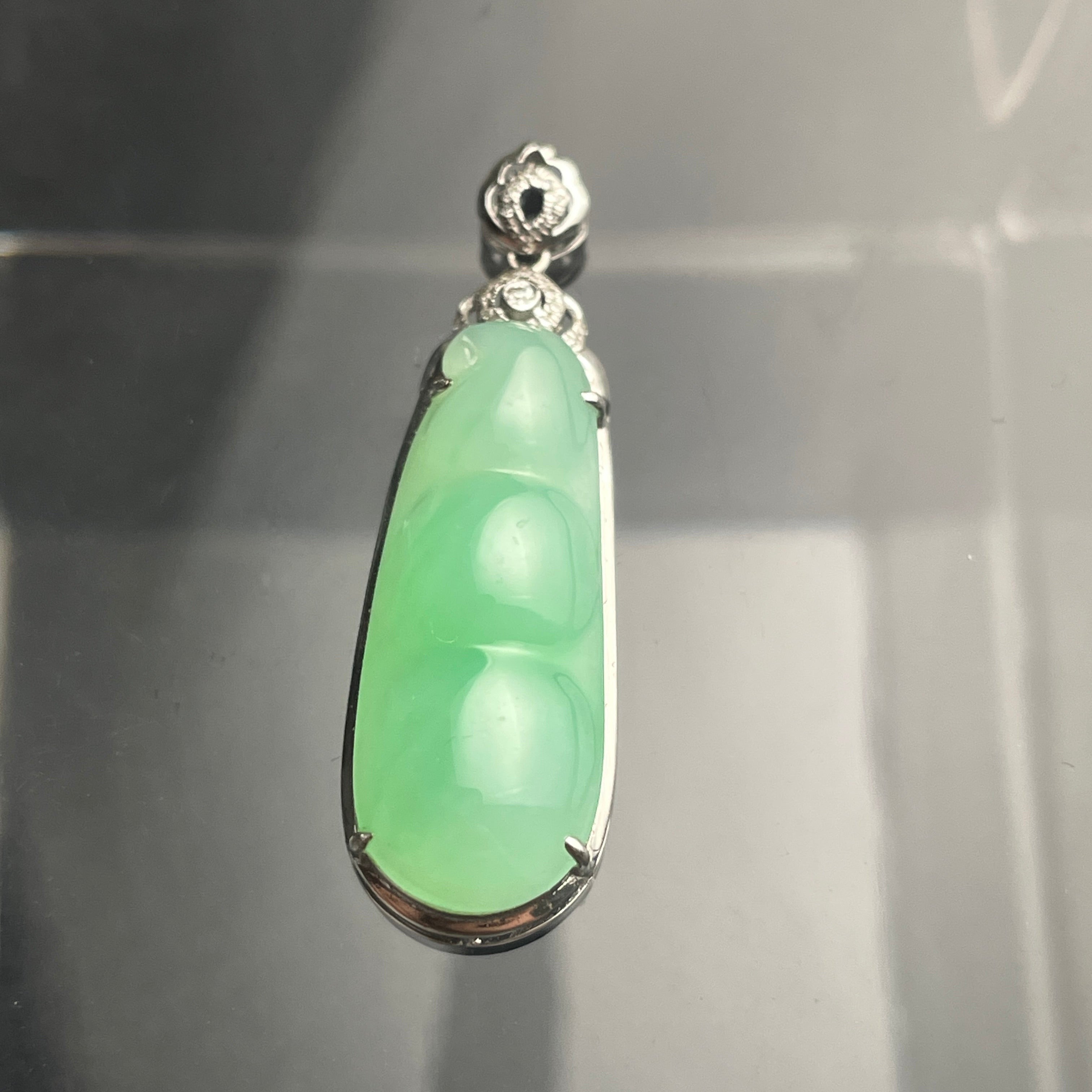 Green carved jadeite pendant set in 18K gold with a floral diamond-accented bail