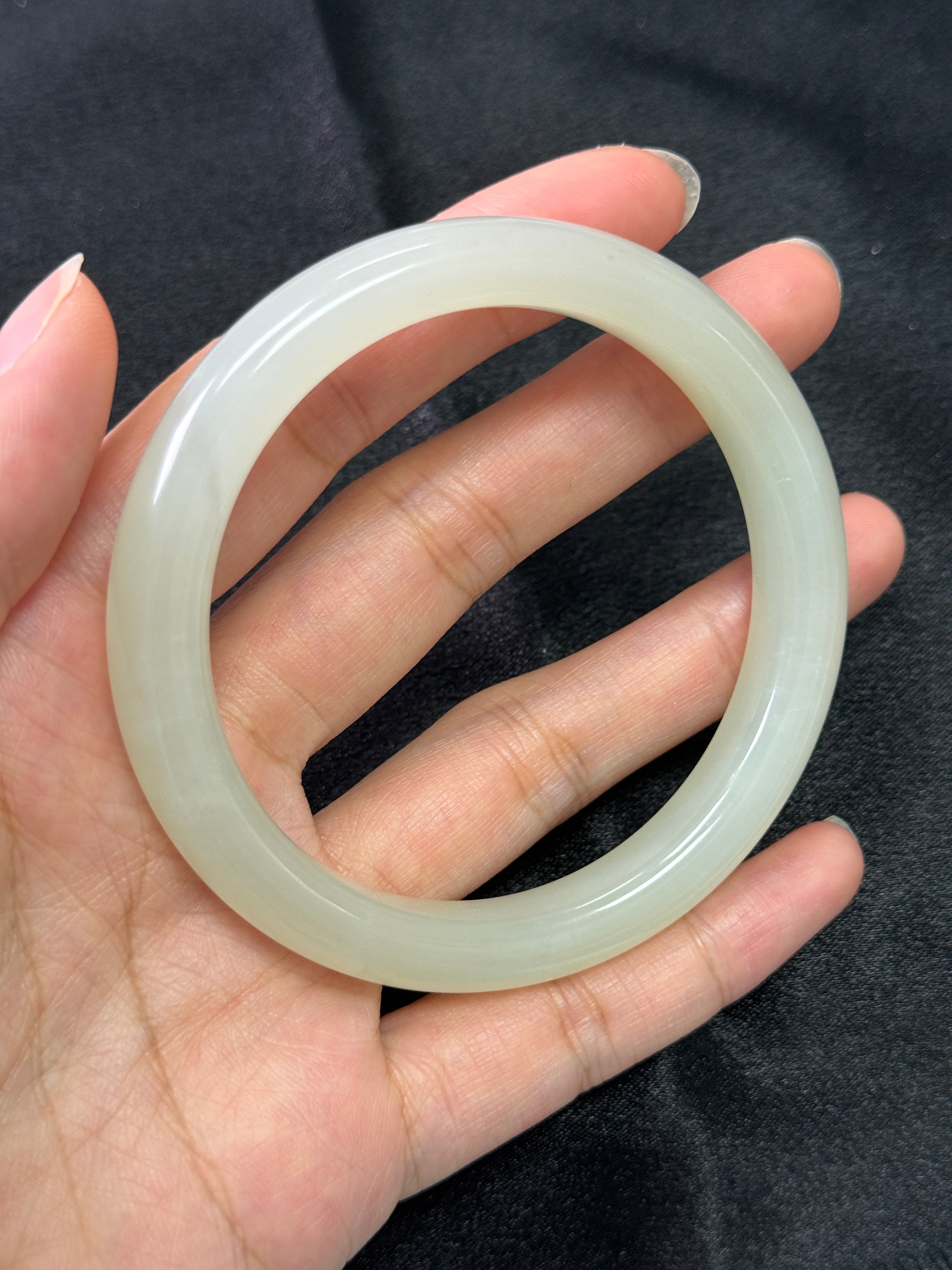 Hand holding a translucent jade bracelet against a dark background