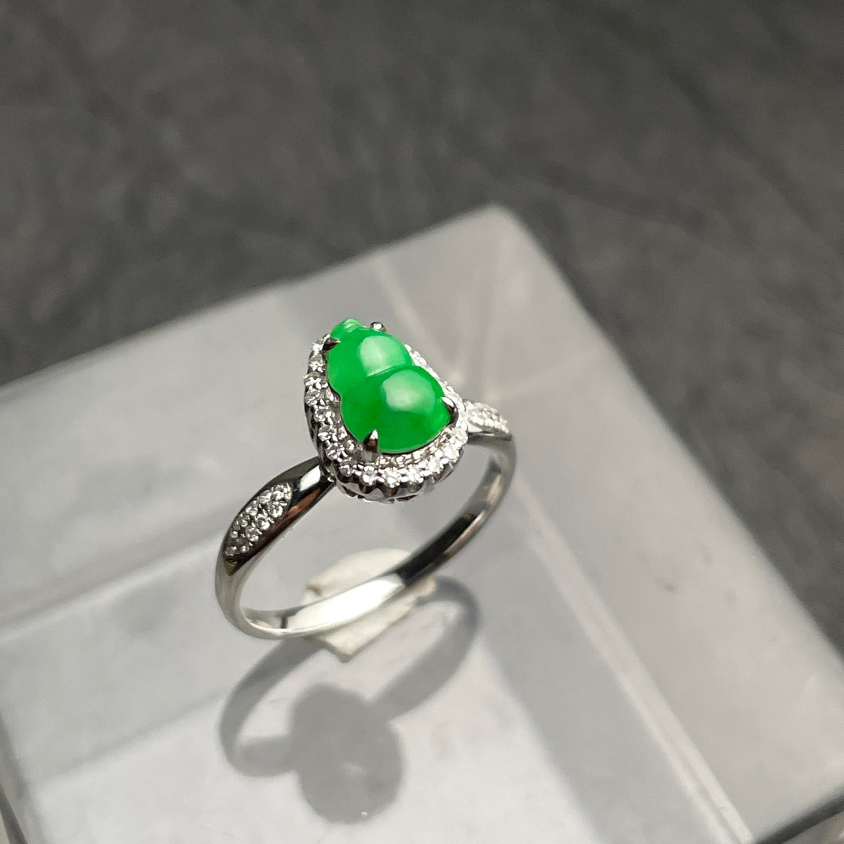 A green carved gourd ring with a clear halo and silver-tone band. Angled view.