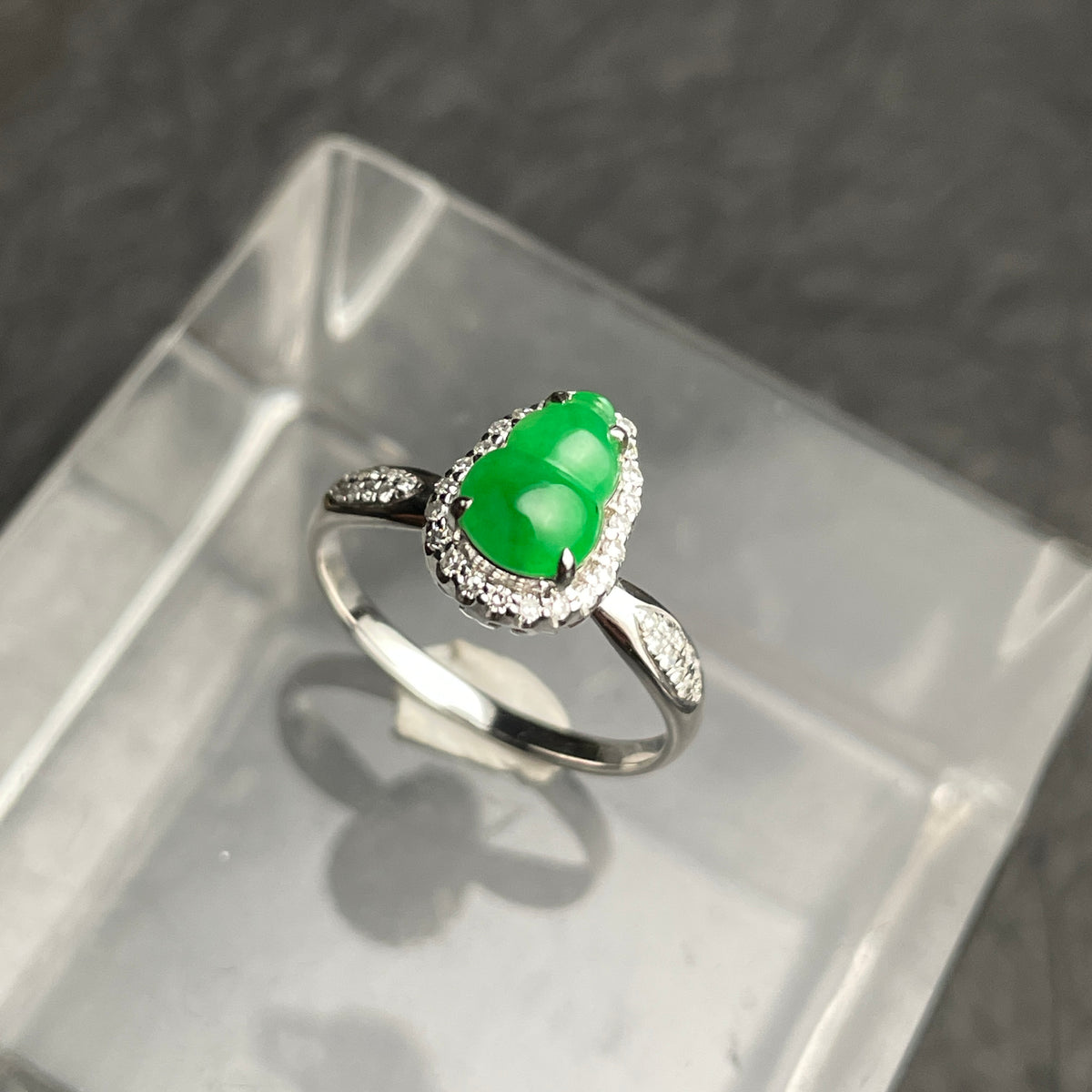 A green carved gourd ring with a clear halo and silver-tone band. Angled view.