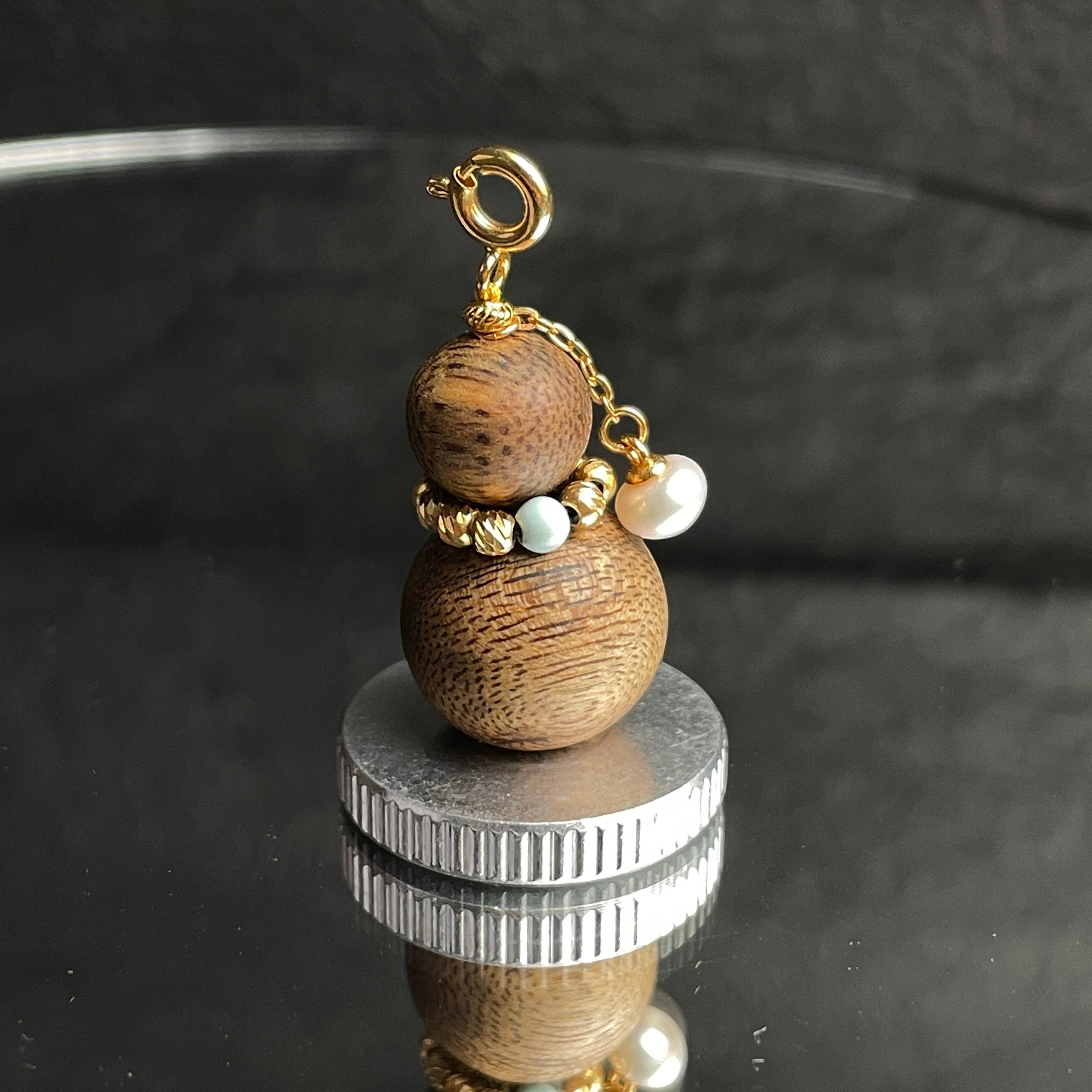Sylvia Jewelry agarwood Wu Lou charm with turquoise bead, freshwater pearl, and gold hardware on a reflective base.