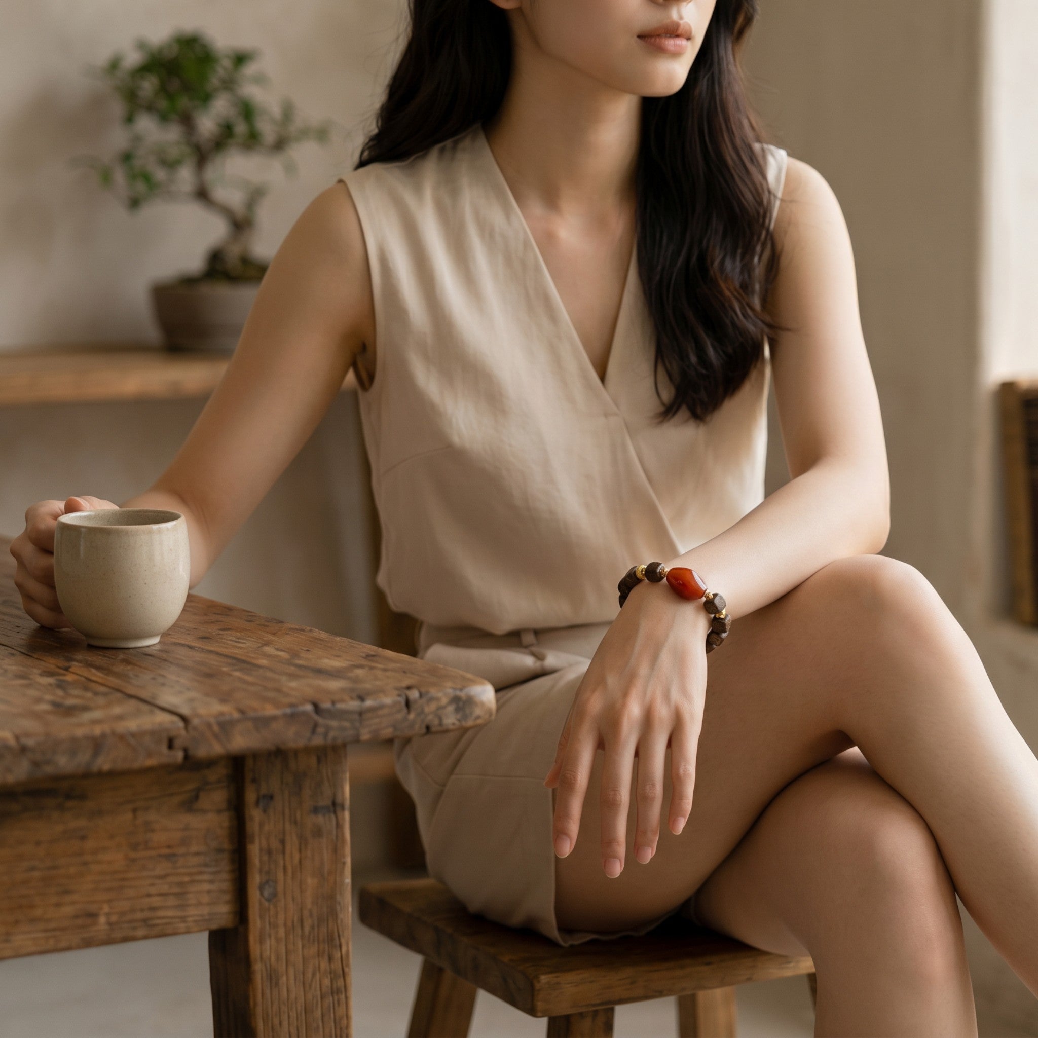 Sylvia Jewelry beaded bracelet with a large red stone worn by a woman in a beige outfit sitting at a wooden table