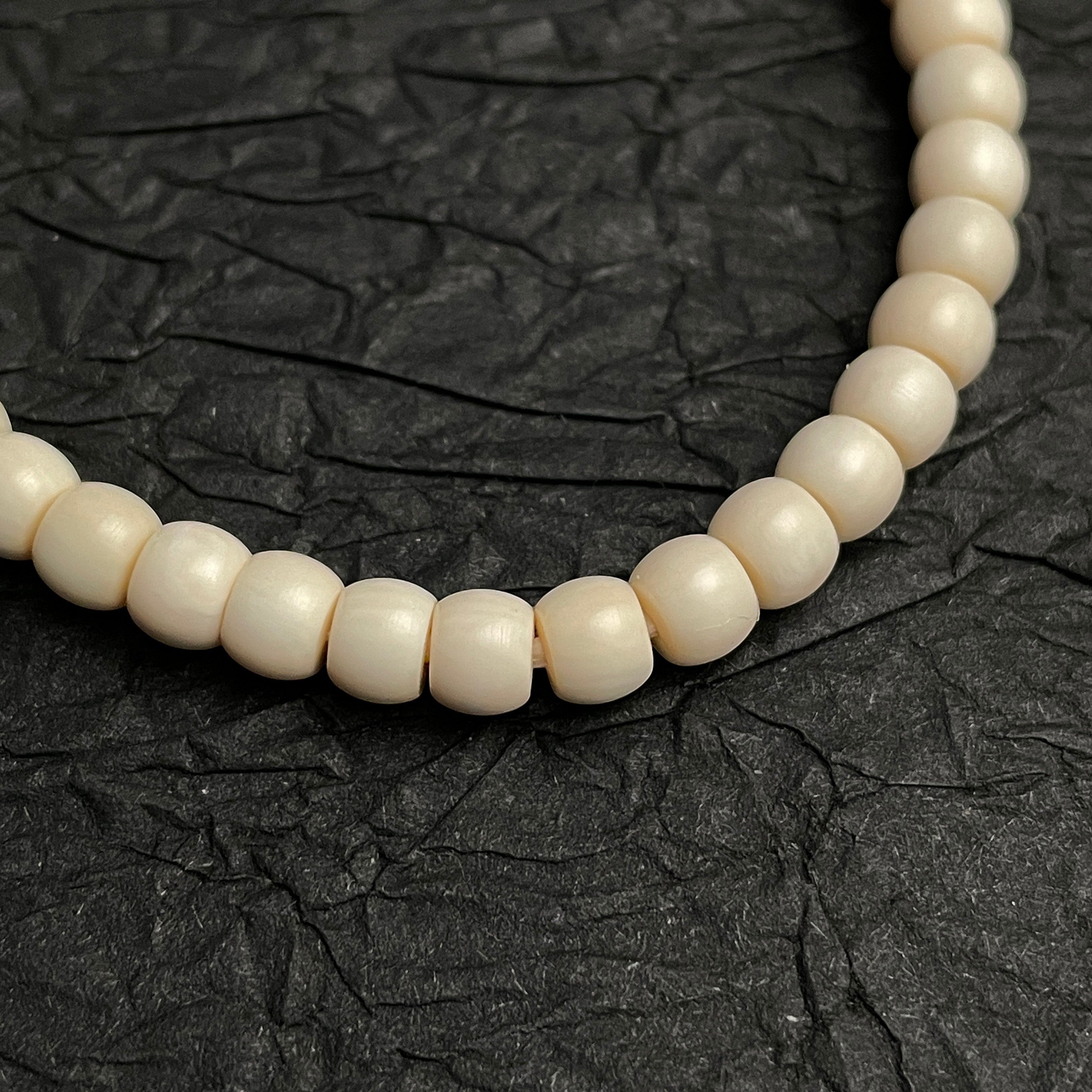 Sylvia Jewelry cream-colored beaded bracelet with smooth, rounded beads on a textured black background.
