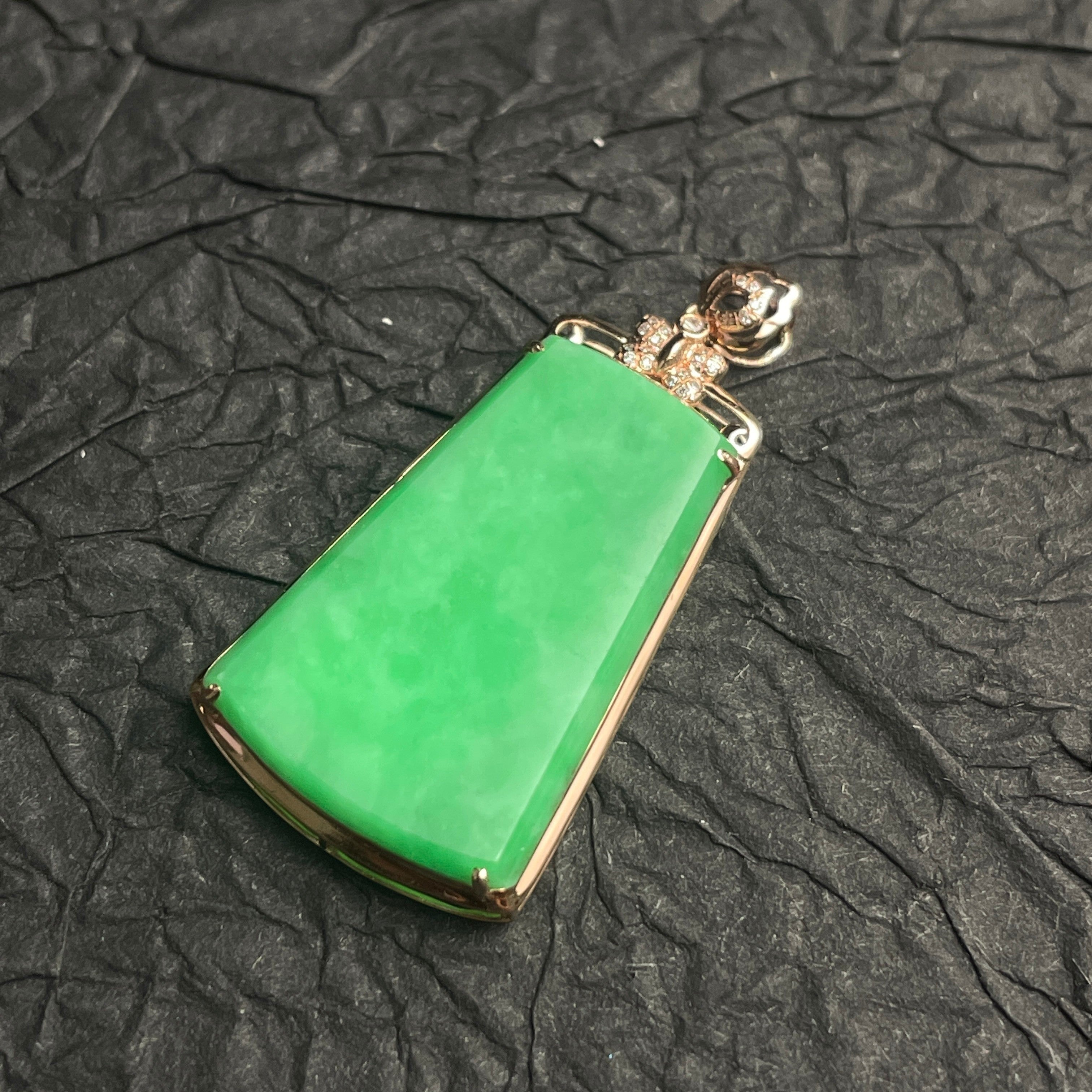 Sylvia Jewelry apple green jadeite trapezoid pendant in 18k gold with diamond pavé accents on a black textured surface.