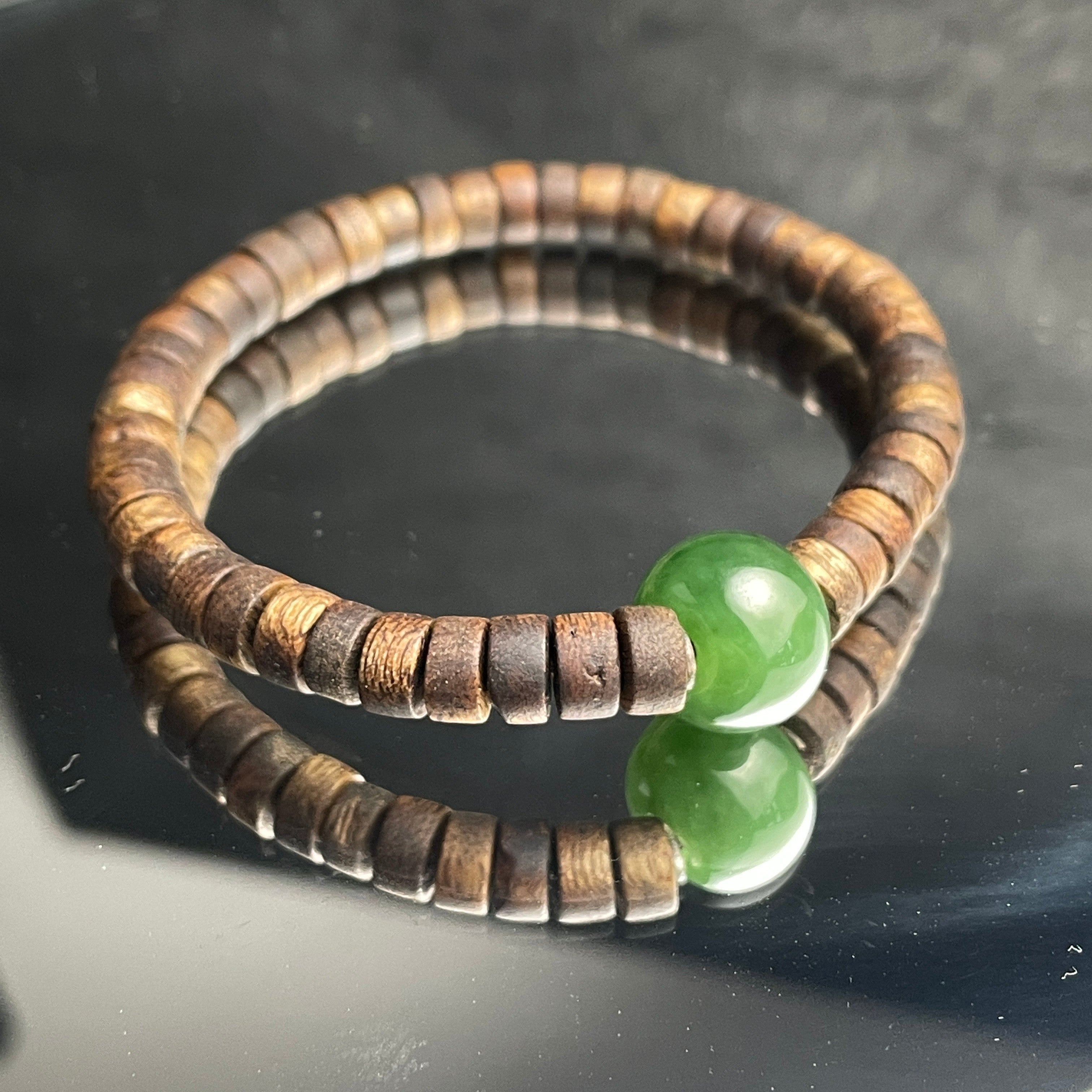 Sylvia Jewelry bracelet featuring a green Hetian nephrite jade bead and natural agarwood abacus spacers on a mirror.