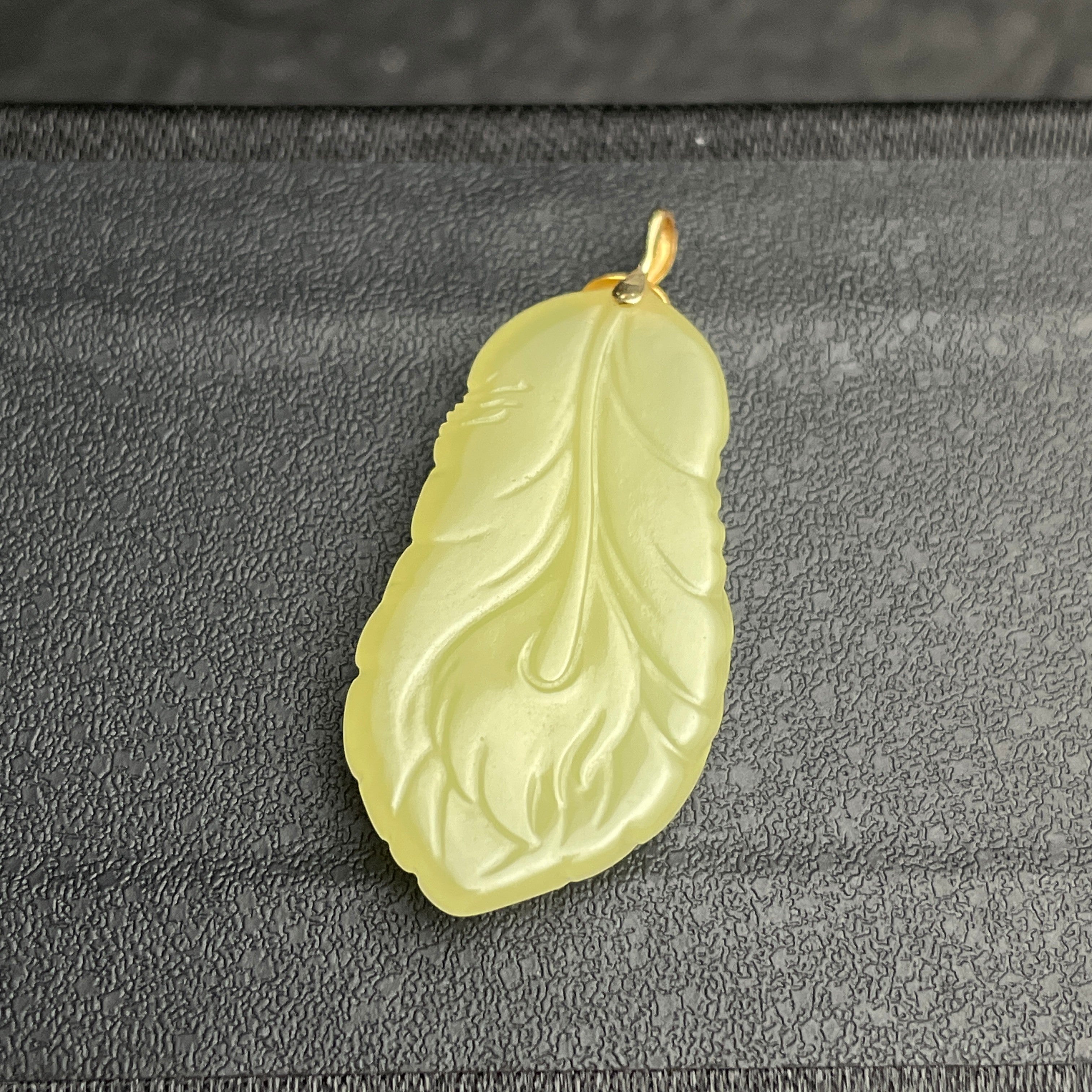 Sylvia Jewelry pale yellow jade feather pendant with gold bail on a textured black background