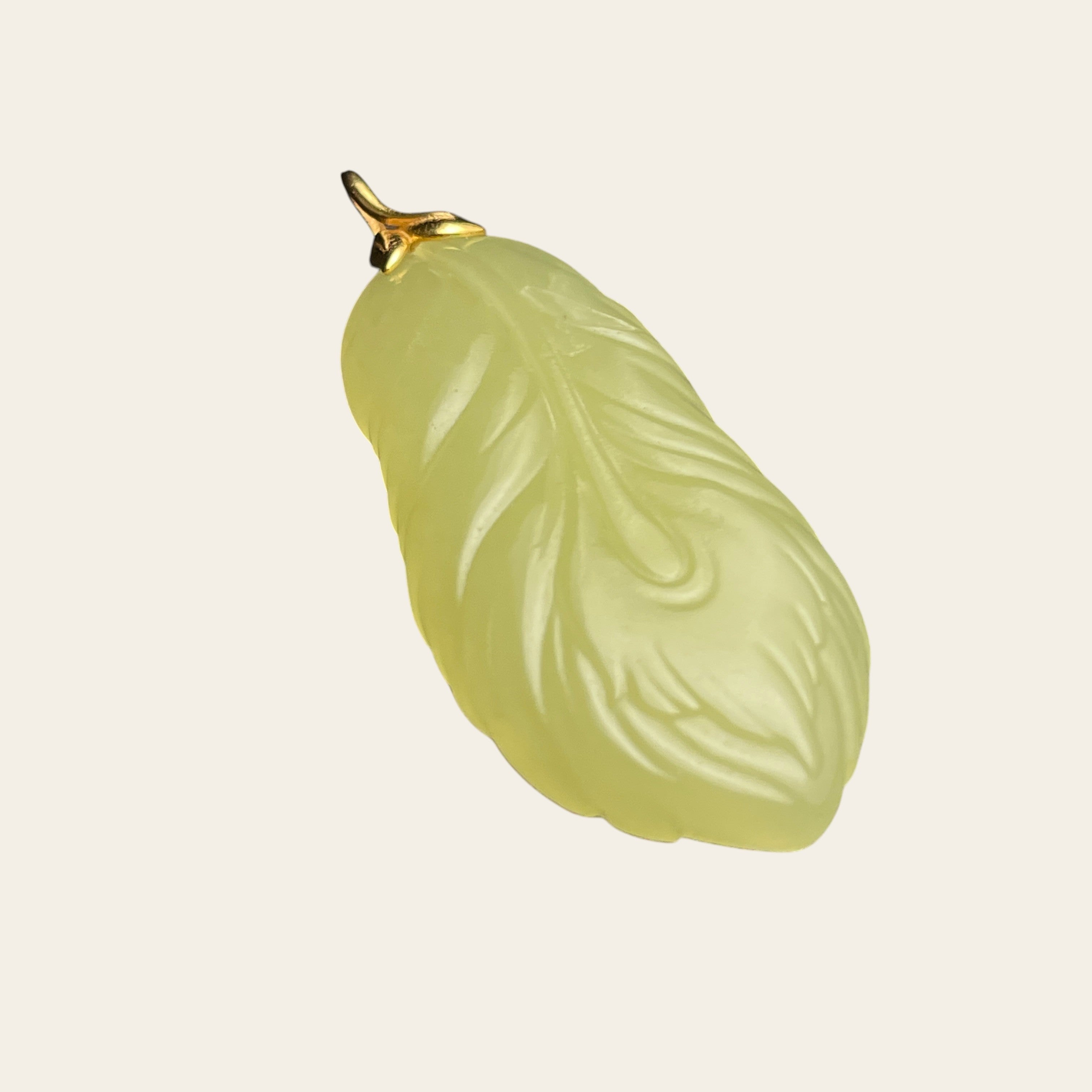 Sylvia Jewelry pale yellow jade feather pendant with gold bail on a textured black background
