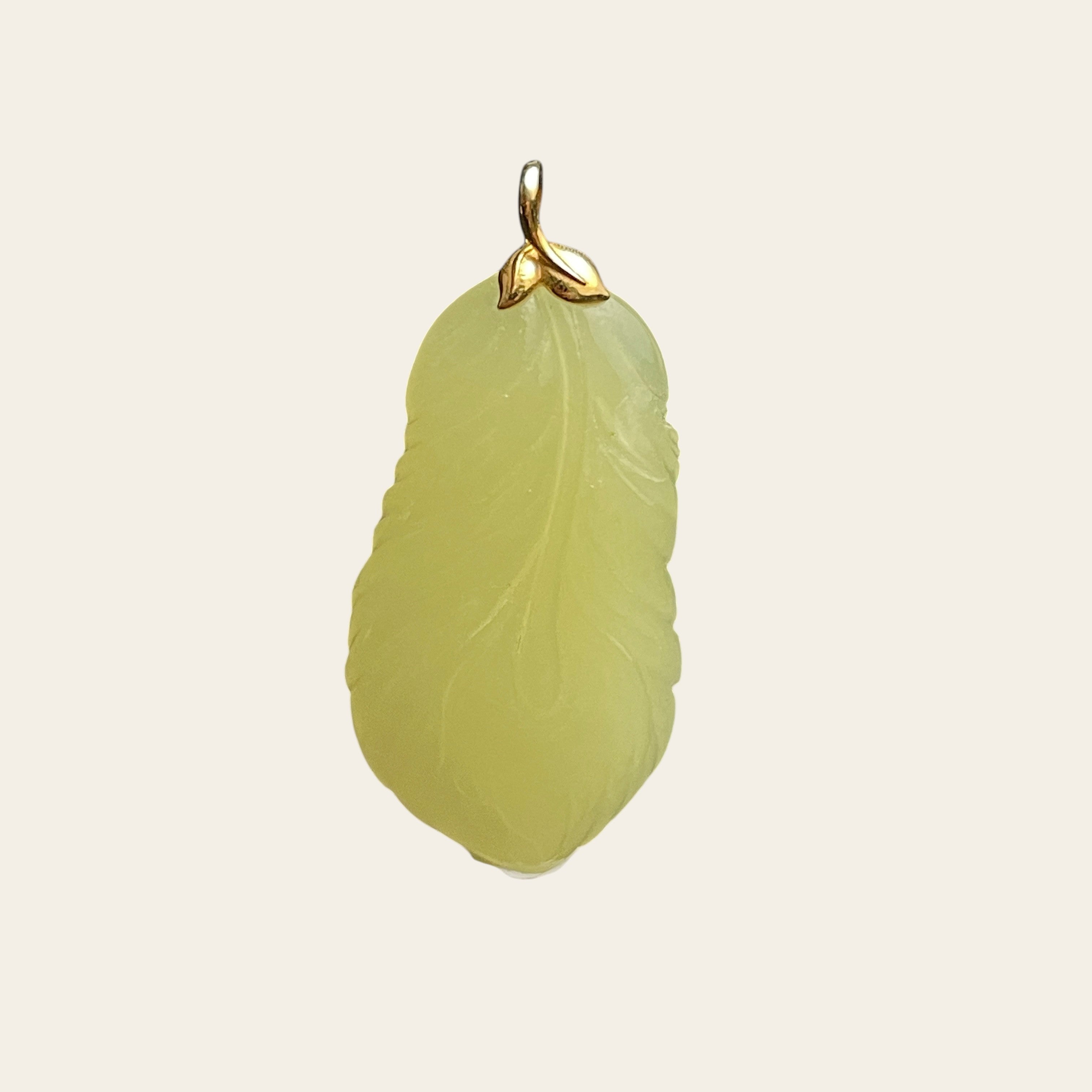 Sylvia Jewelry pale yellow jade feather pendant with a delicate gold bail on a dark textured background.