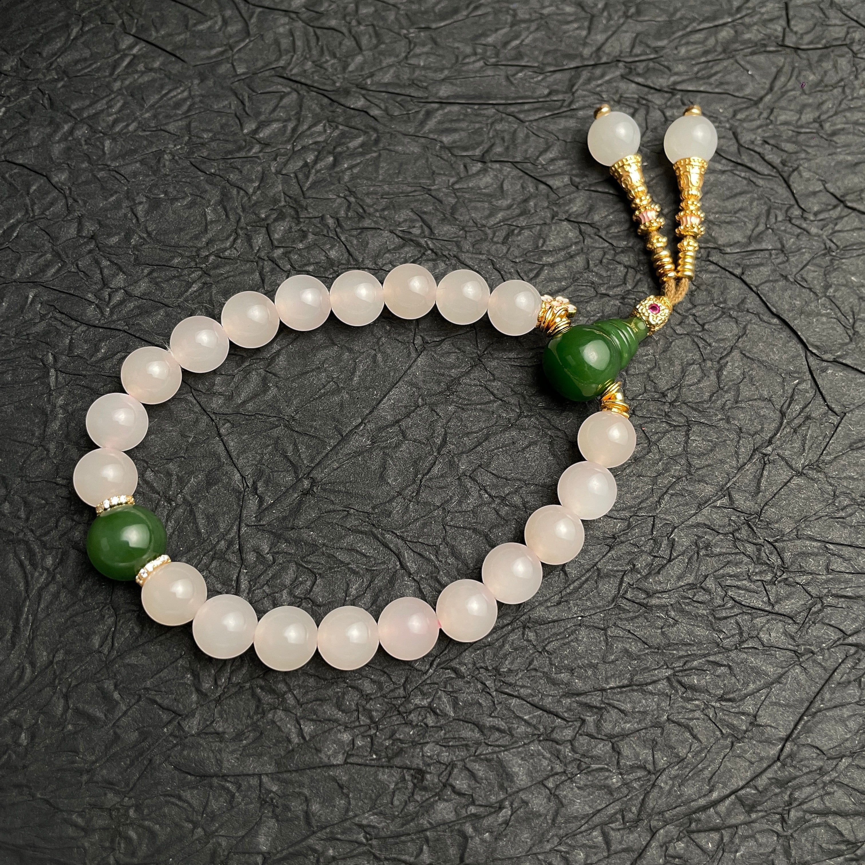 Sylvia Jewelry 粉色水晶串珠手链,搭配绿色玉石吊坠和金色流苏装饰。