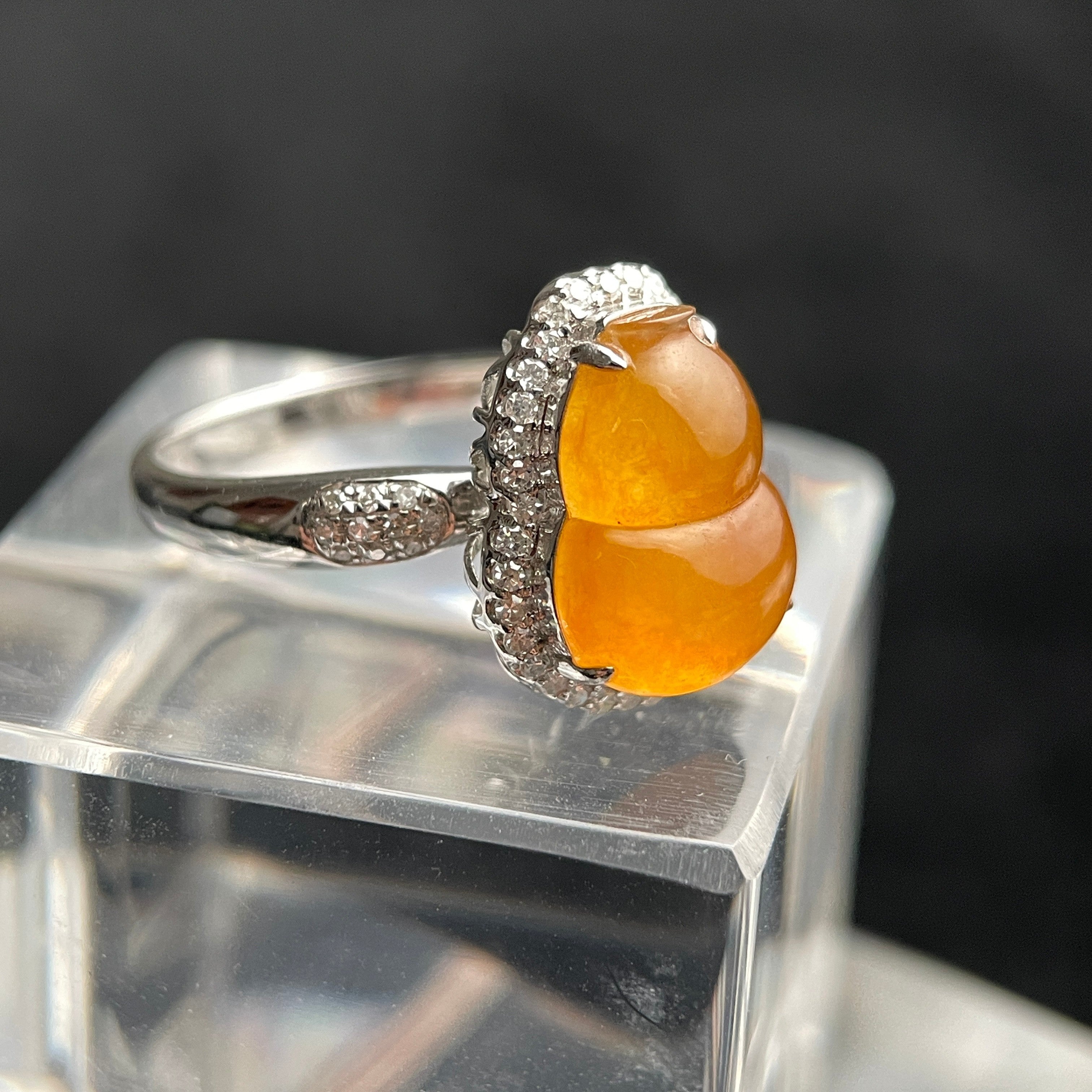 Sylvia Jewelry yellow jadeite double-gourd ring with diamond halo and 18K white gold band on a clear display block.
