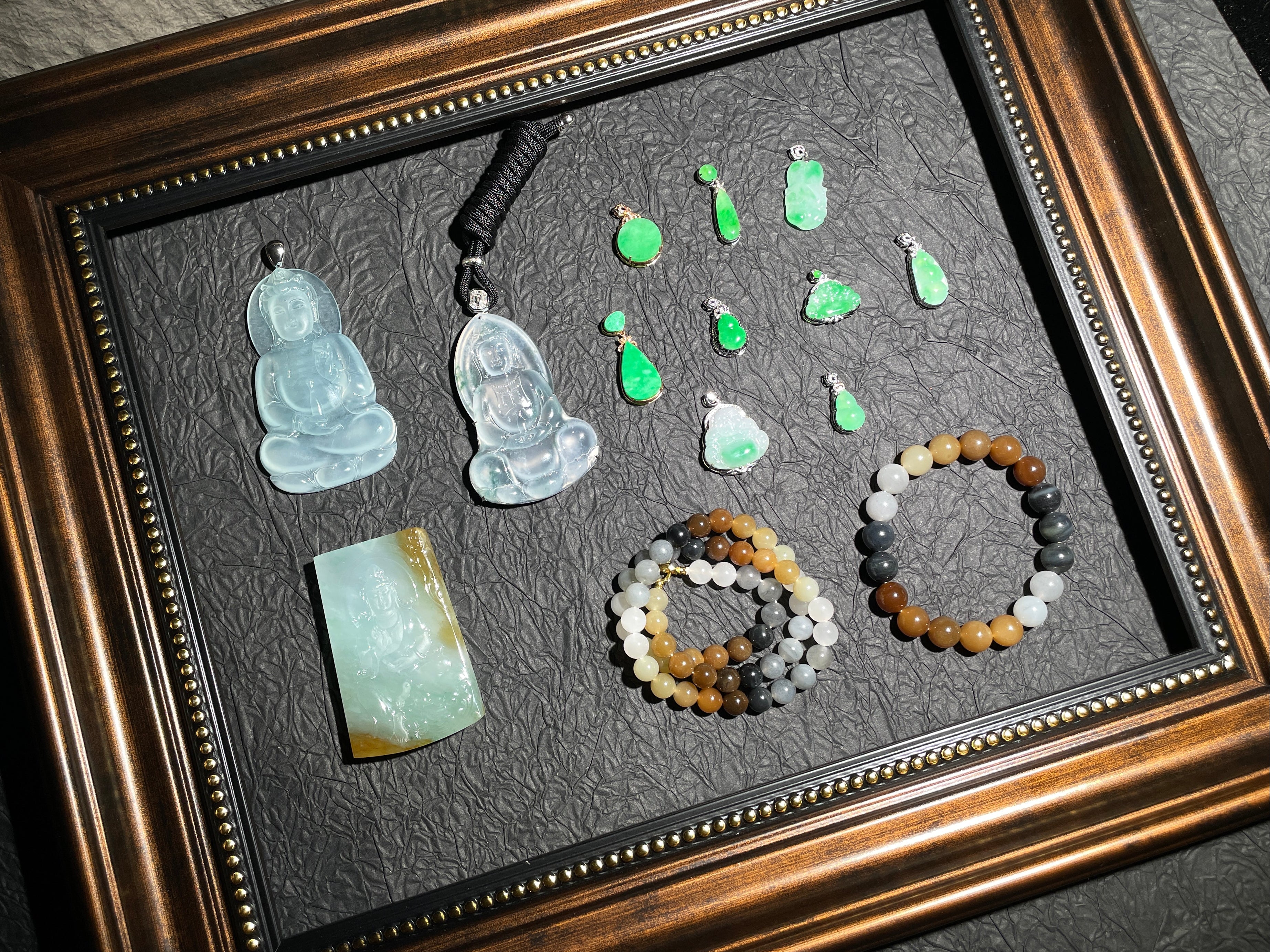 Framed display of jade jewelry including pendants and bracelets on a dark background.