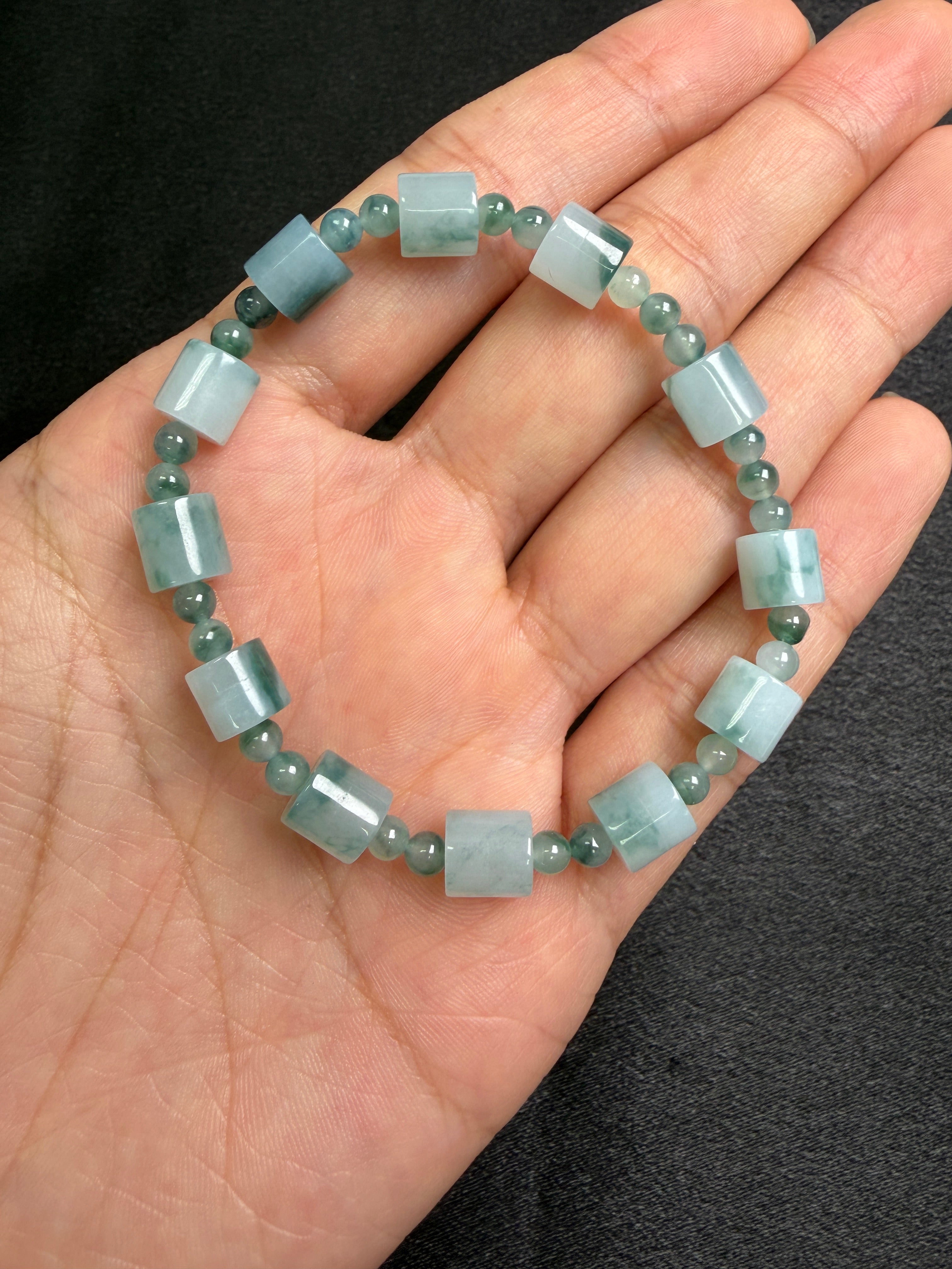Hand holding a bracelet with light blue and green jadeite beads against a dark background