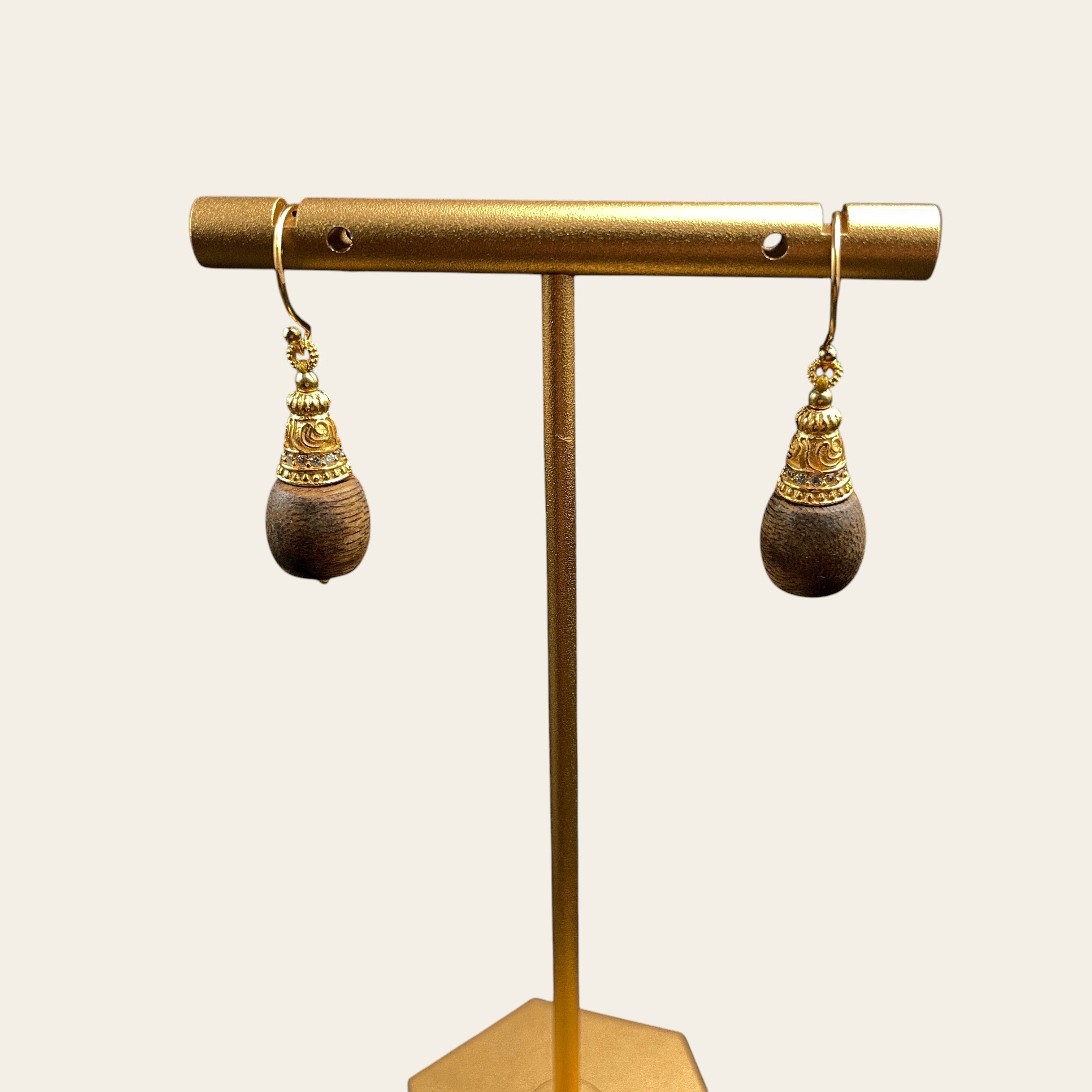 Sylvia Jewelry agarwood drop earrings with crystal-paved gold filigree caps hanging on a gold display stand.