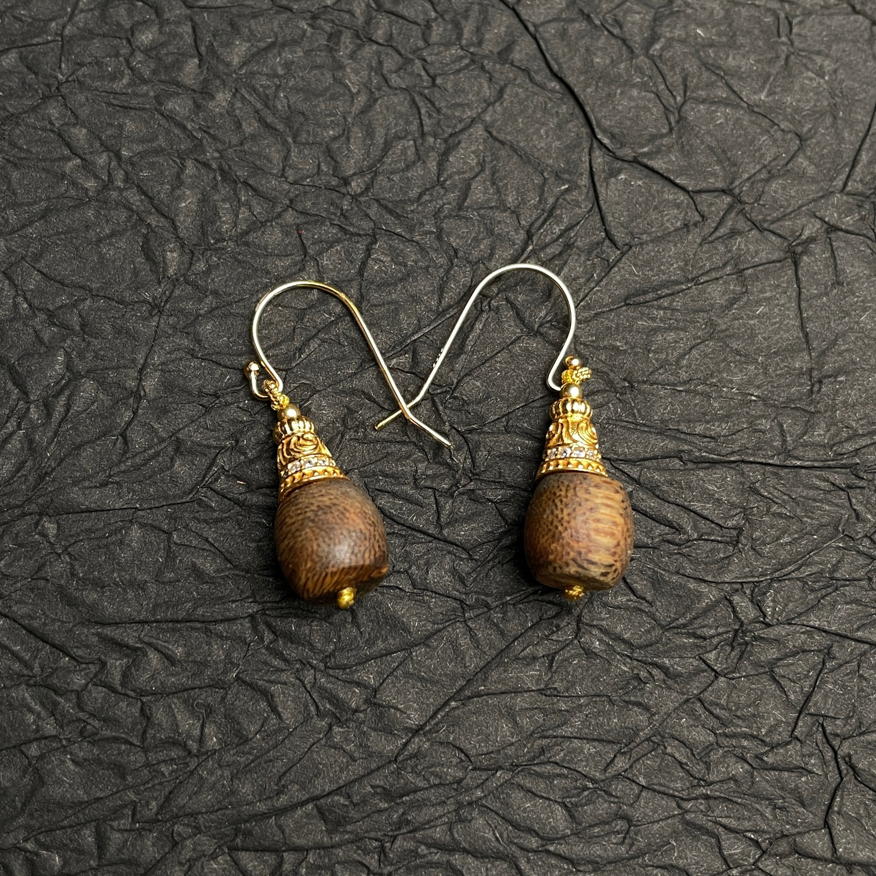 Sylvia Jewelry Zen Drop agarwood earrings with crystal-paved gold filigree caps and gold wire hooks on black texture