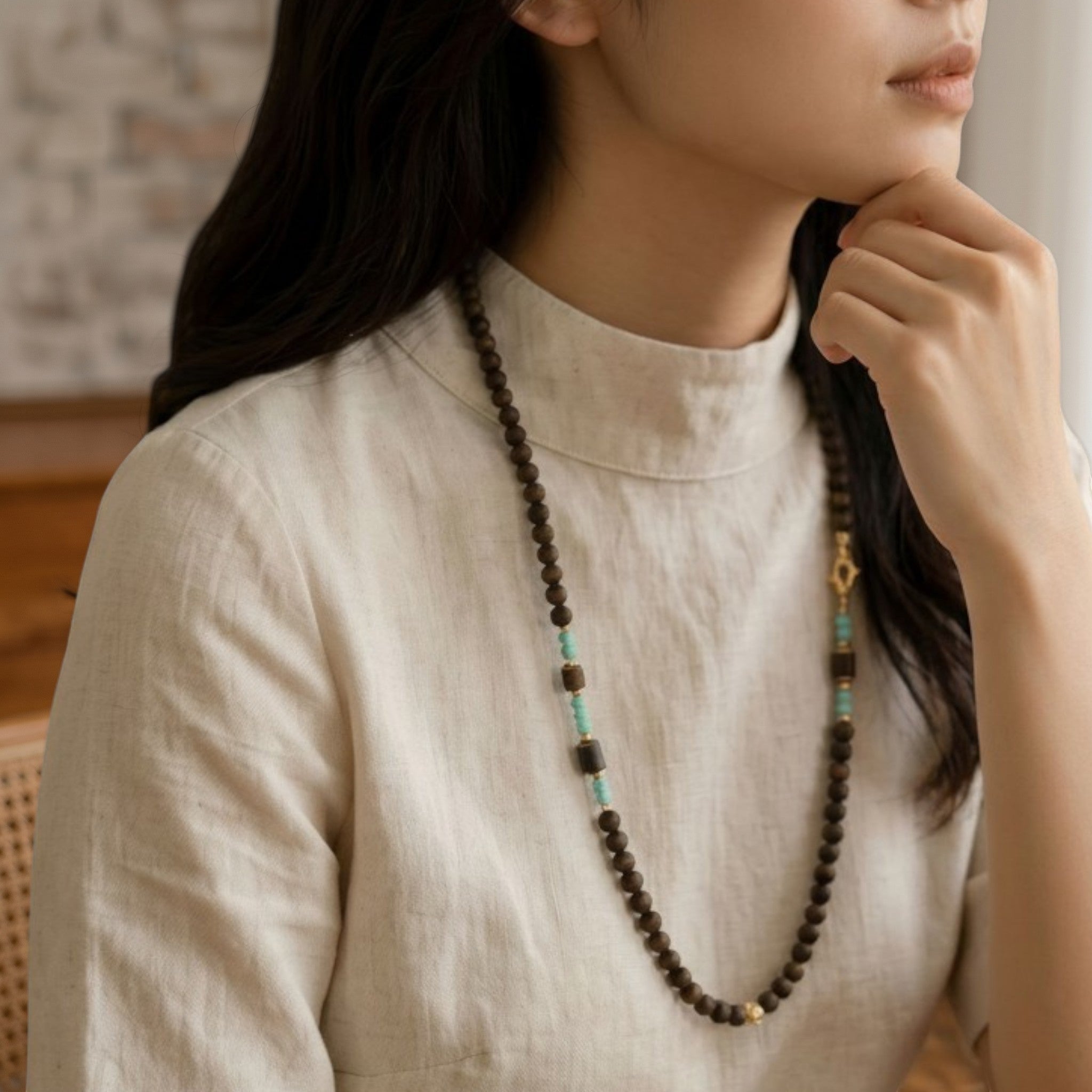 Sylvia Jewelry long necklace featuring natural agarwood beads and turquoise accents worn by a woman in a linen top.
