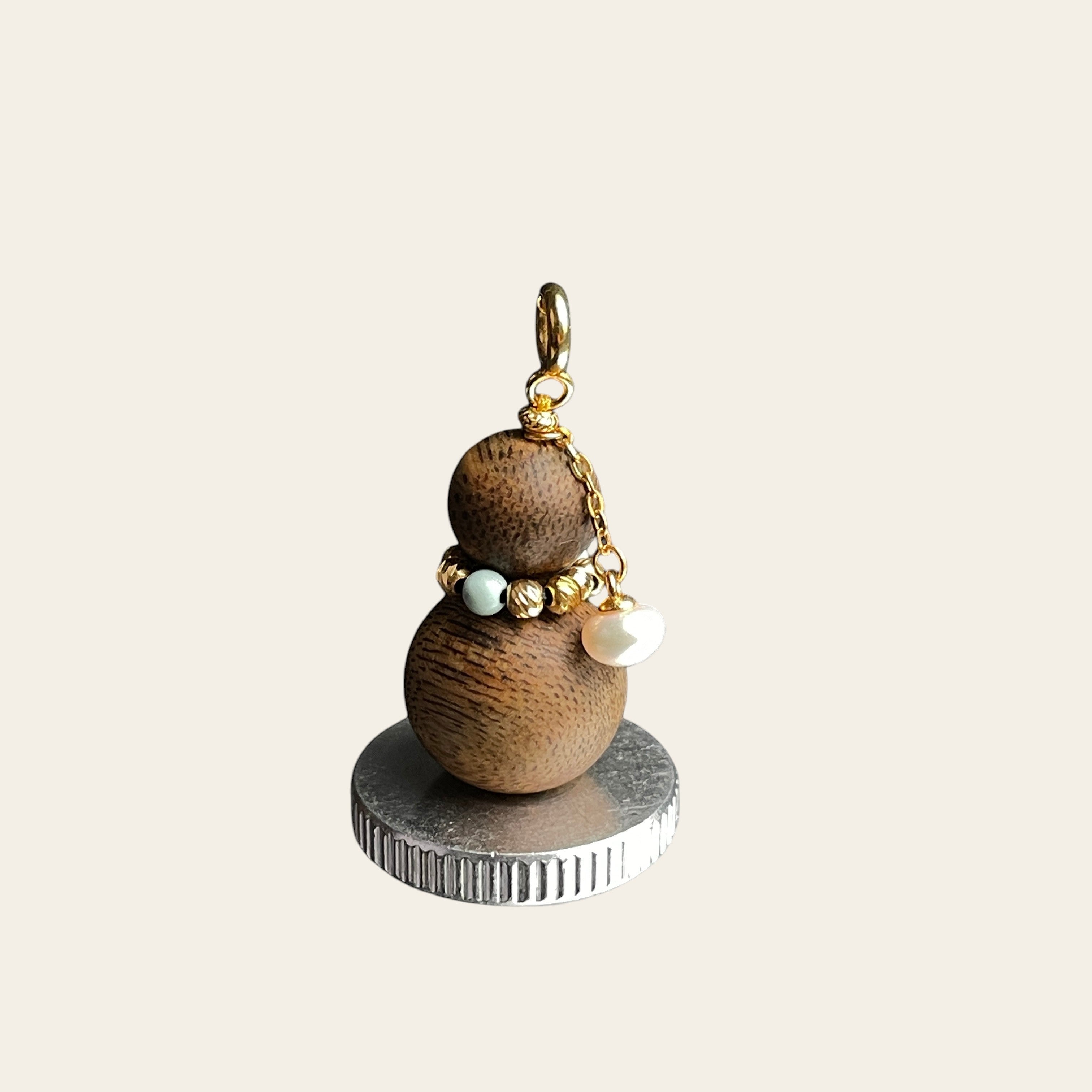 Sylvia Jewelry aromatic agarwood Wu Lou charm with turquoise bead, freshwater pearl, and gold hardware on a display base.