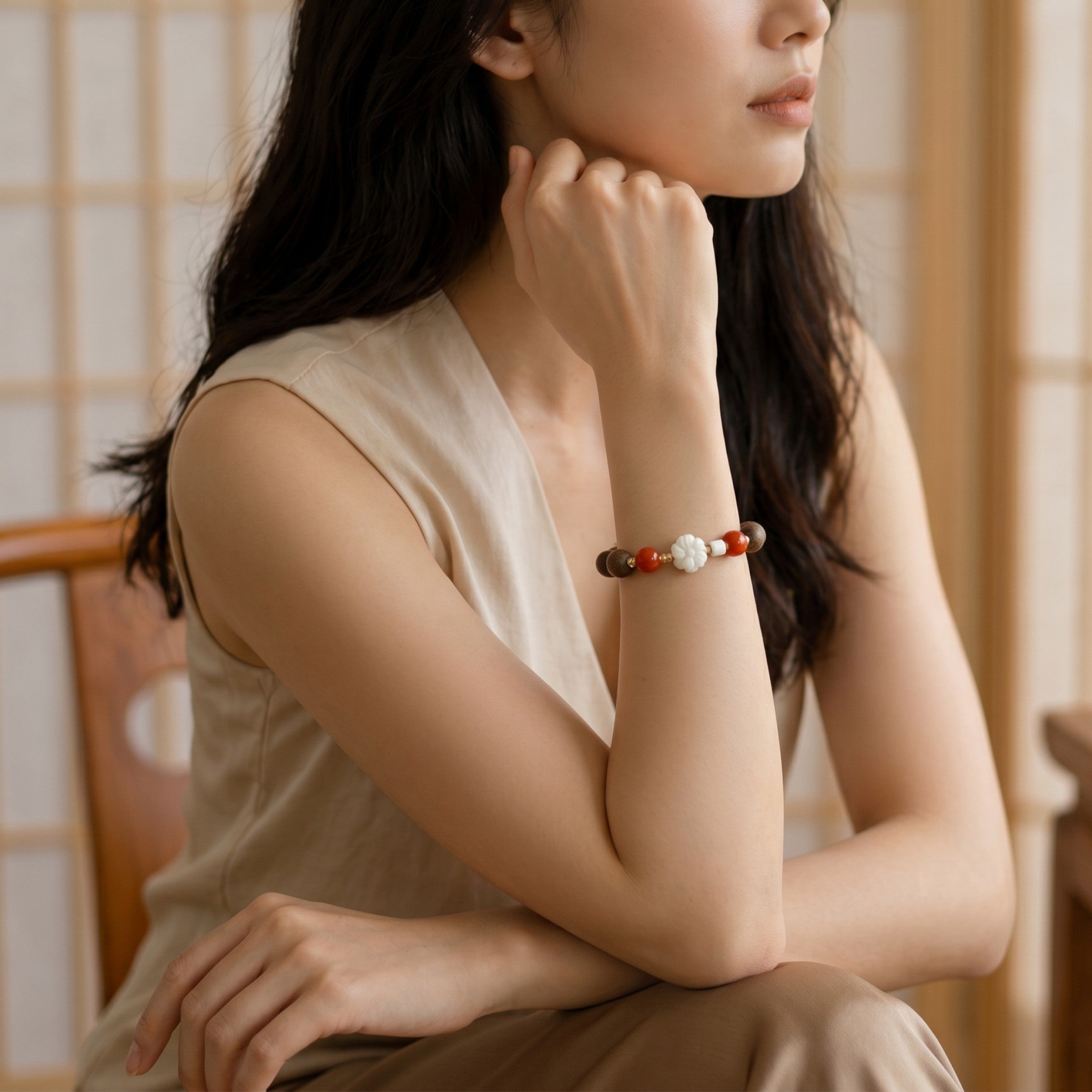 Sylvia Jewelry bracelet with white flower charm and red beads worn by a woman in a serene indoor setting