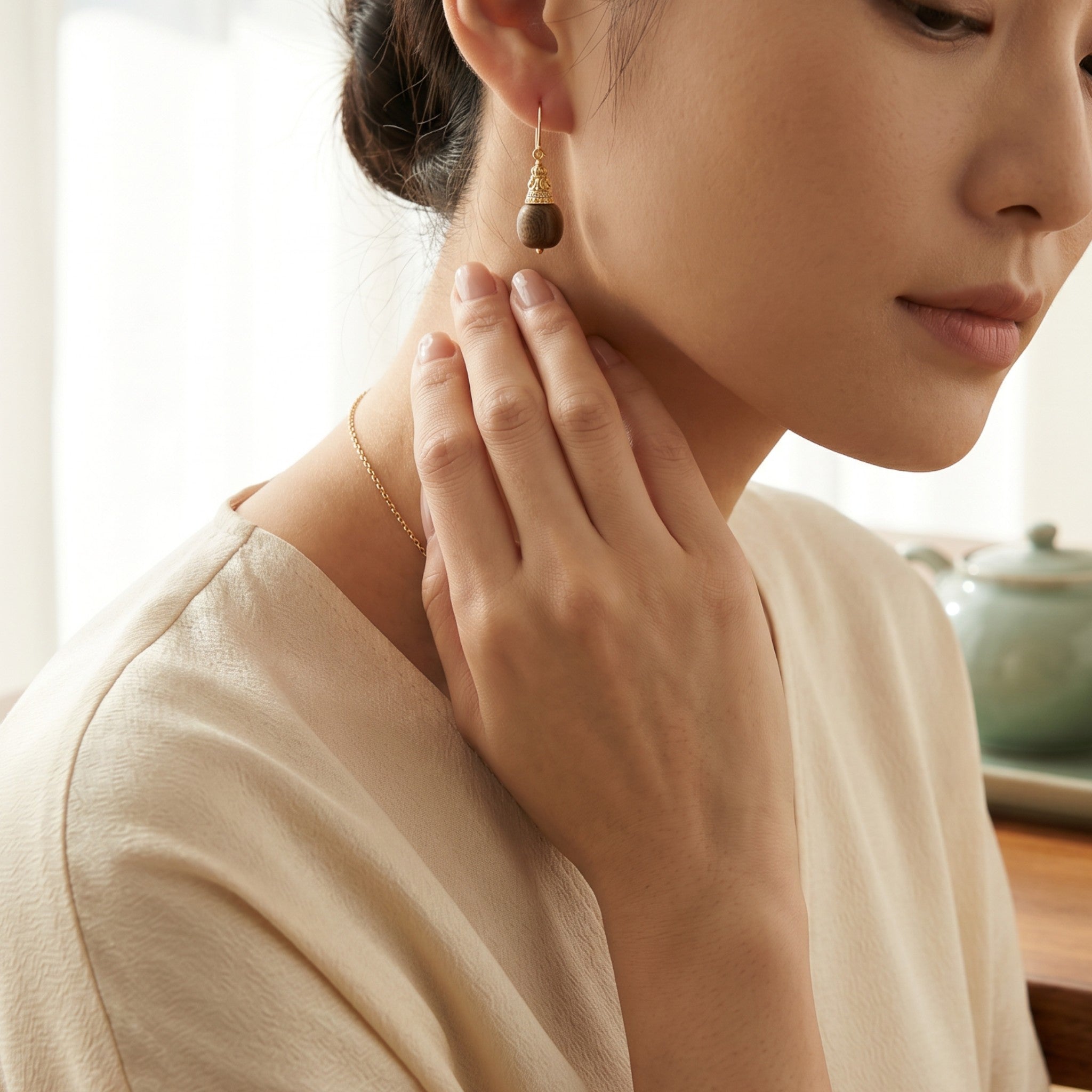 Sylvia Jewelry gold drop earrings with dark wood beads worn by a woman in a serene tea room setting