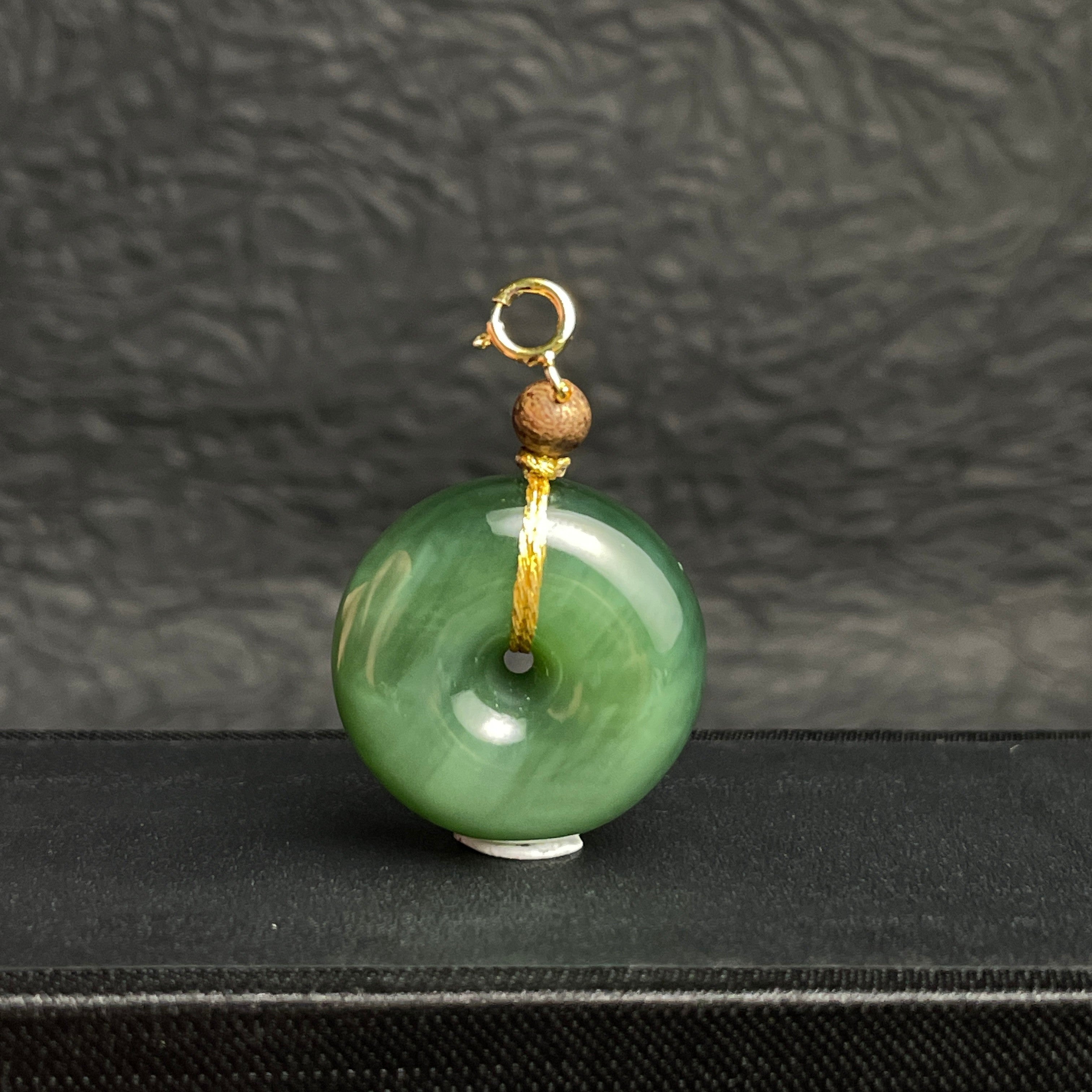 Sylvia Jewelry green jade donut pendant with a gold clasp and small wooden bead accent on a black display stand.