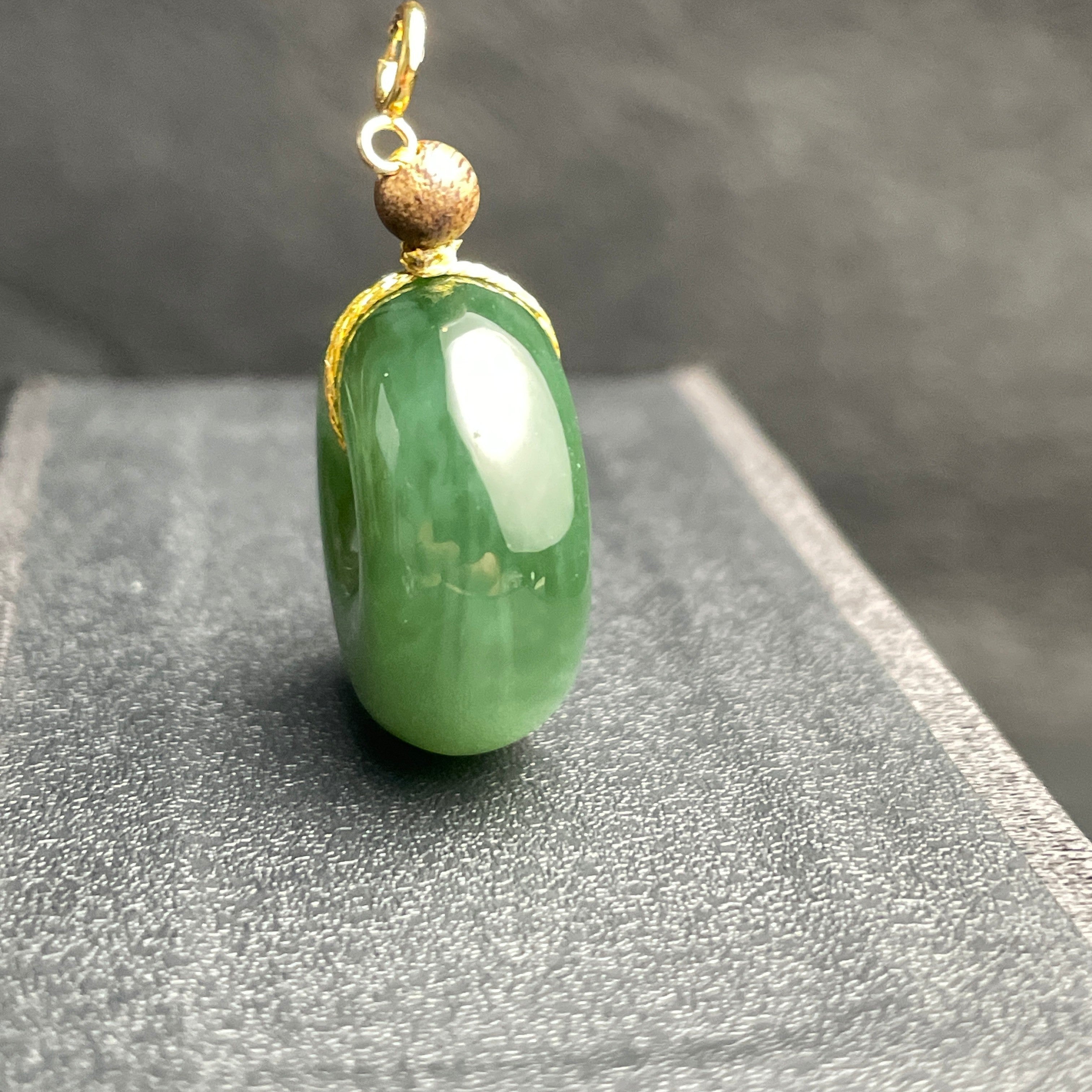 Sylvia Jewelry green jade donut pendant with a gold bail and textured gold bead accent on a dark display stand.