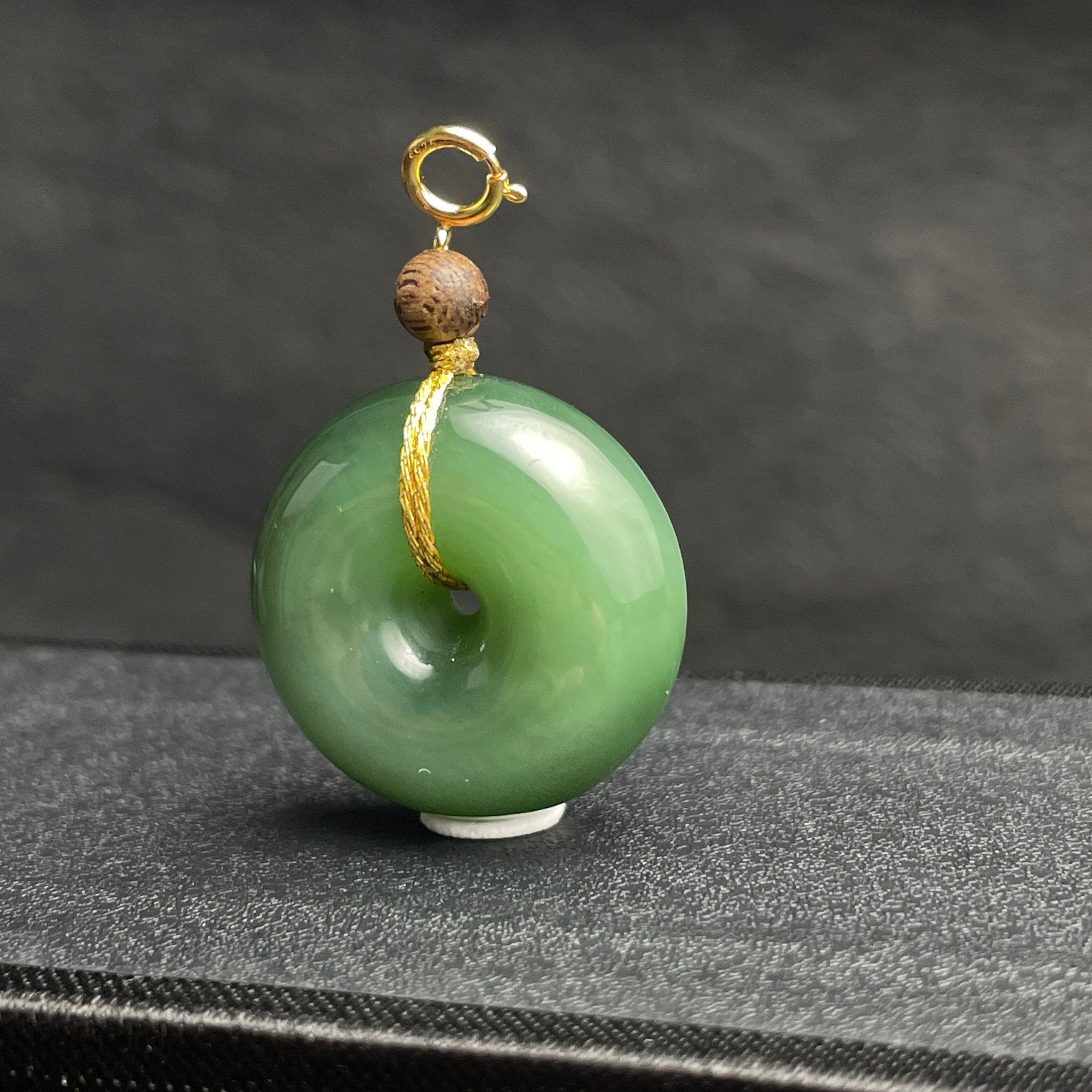 Sylvia Jewelry green jade donut pendant with a small wooden bead and gold clasp on a dark textured background