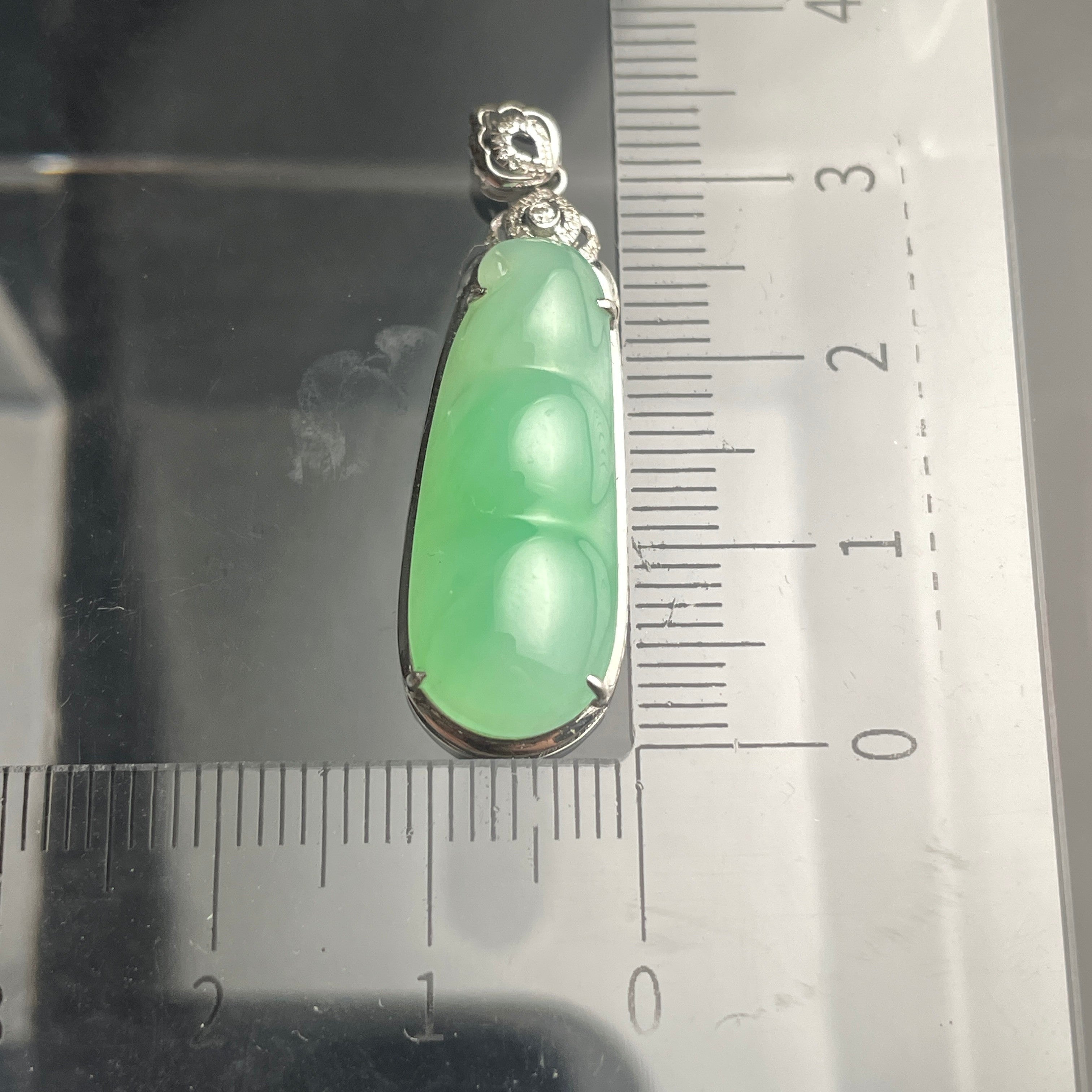 Sylvia Jewelry 18K gold green jadeite bean pendant with a floral diamond-accented bail on a measuring scale.