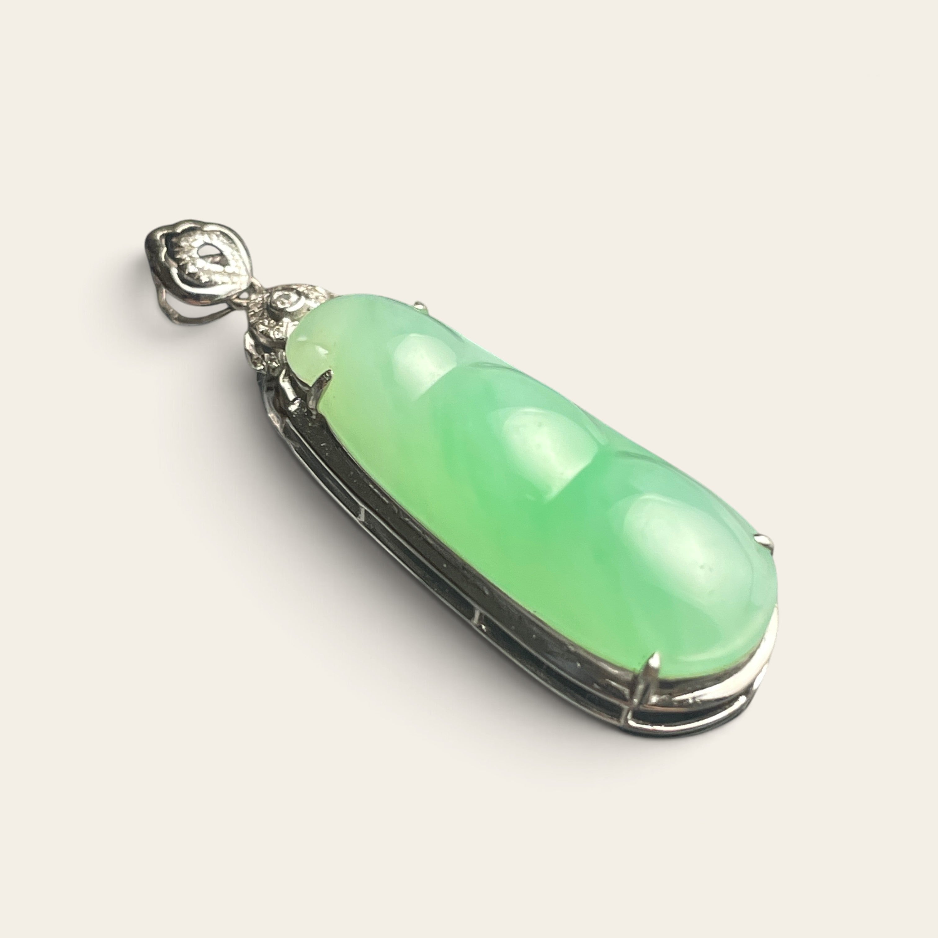 Sylvia Jewelry 18K gold green jadeite bean pendant with a diamond-accented floral bail on a reflective surface.