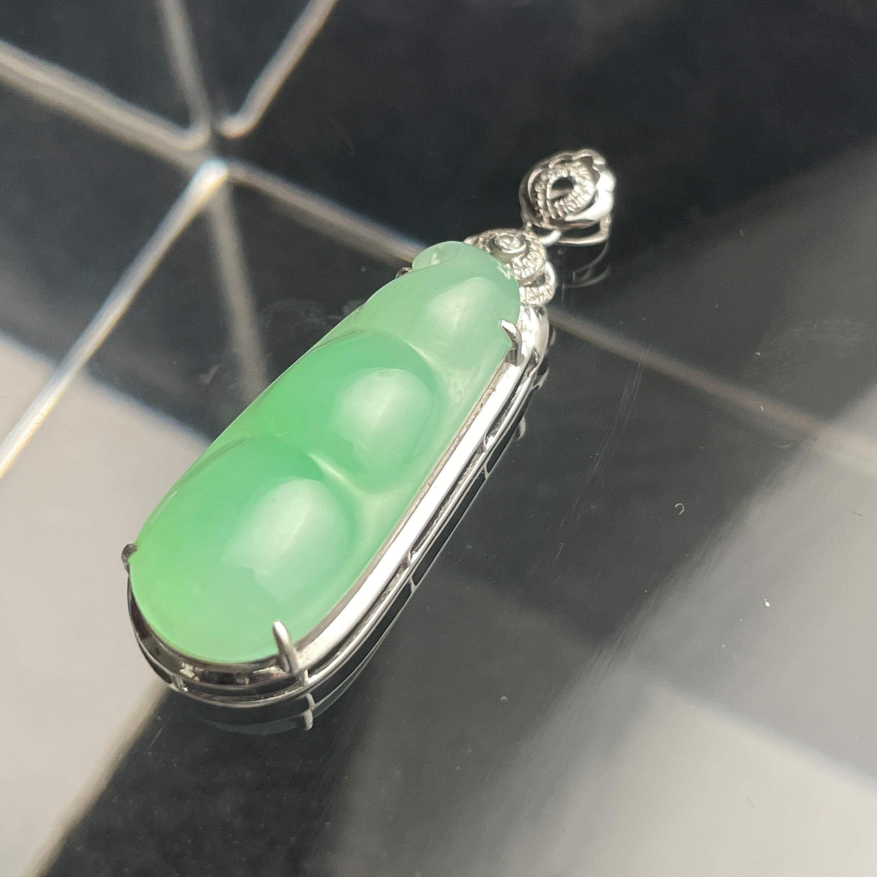 Sylvia Jewelry 18K gold green jadeite bean pendant with a floral diamond-accented bail on a reflective surface.