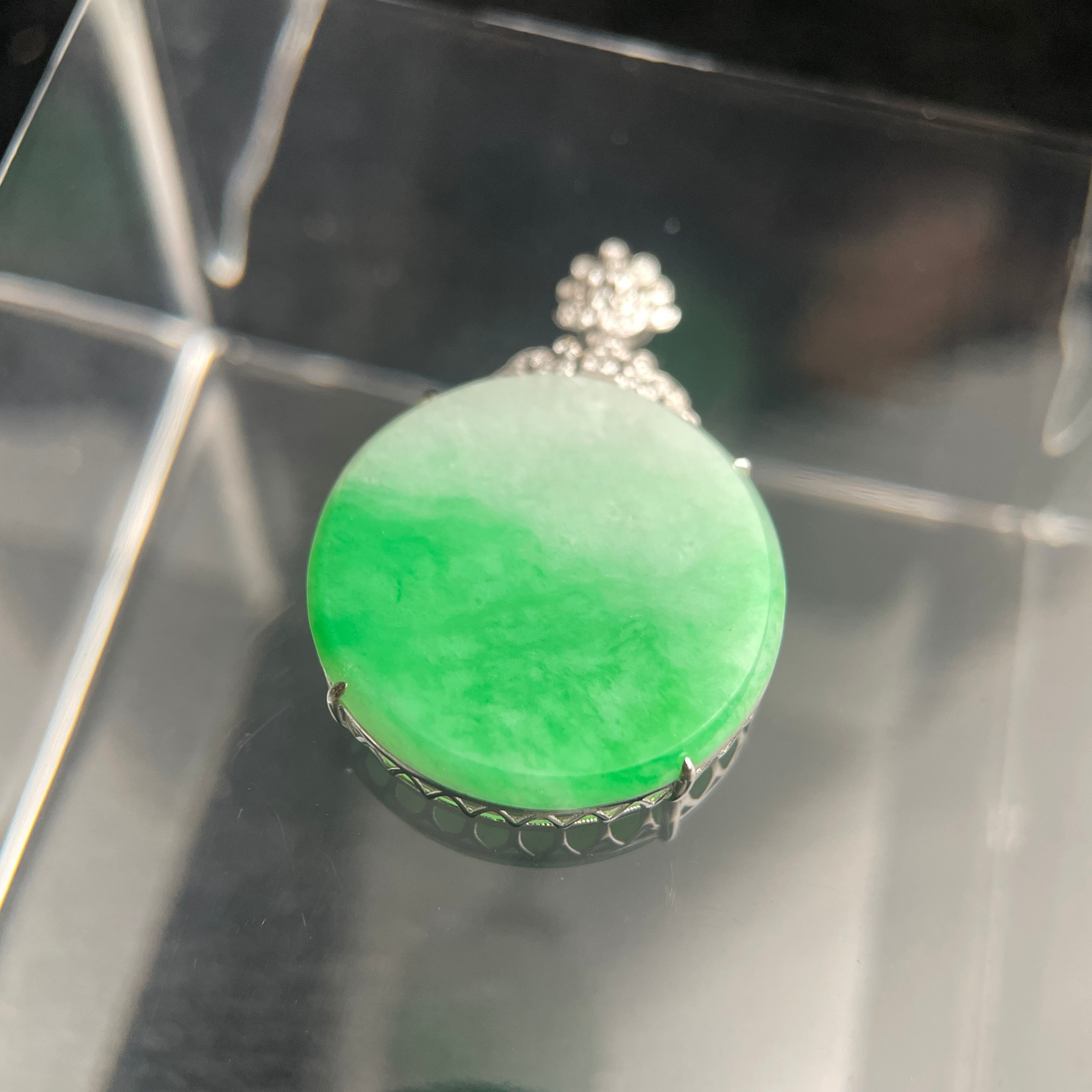 Sylvia Jewelry bright green jadeite jade pendant plaque in a polished 18K gold setting on a reflective surface.