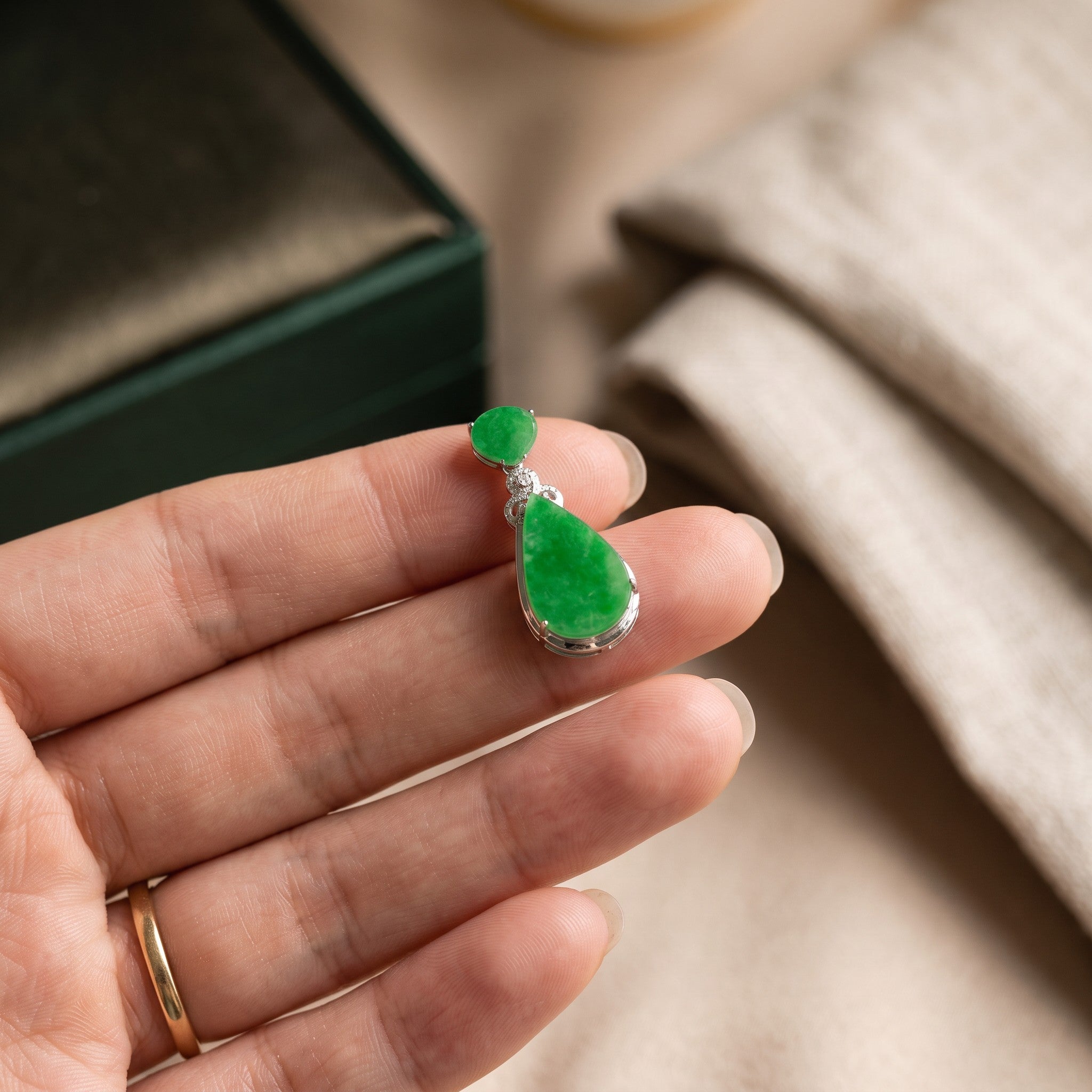 Sylvia Jewelry emerald green jadeite teardrop pendant with diamond accents set in 18K gold held in a hand