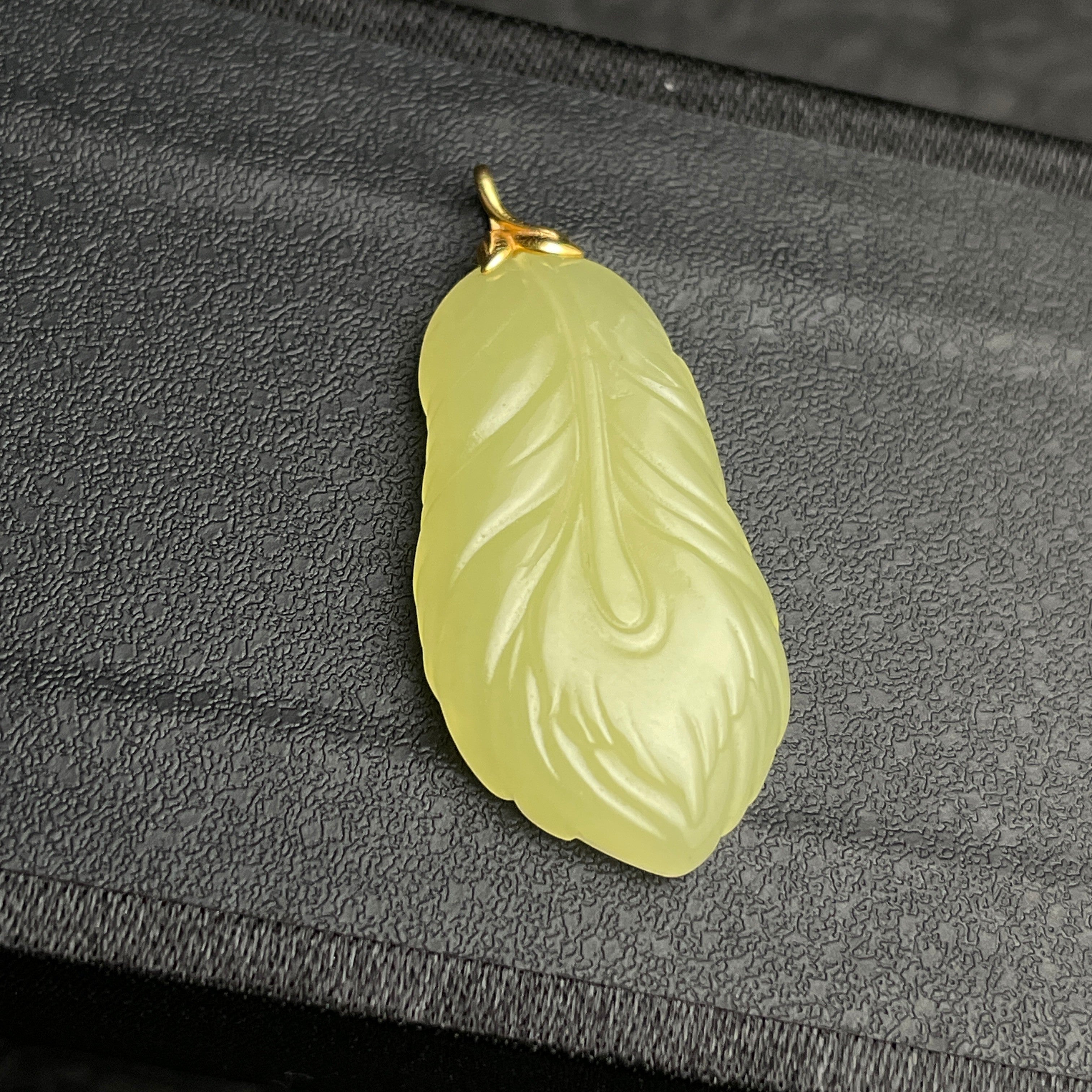 Sylvia Jewelry pale yellow jade feather pendant with gold bail on a textured black background