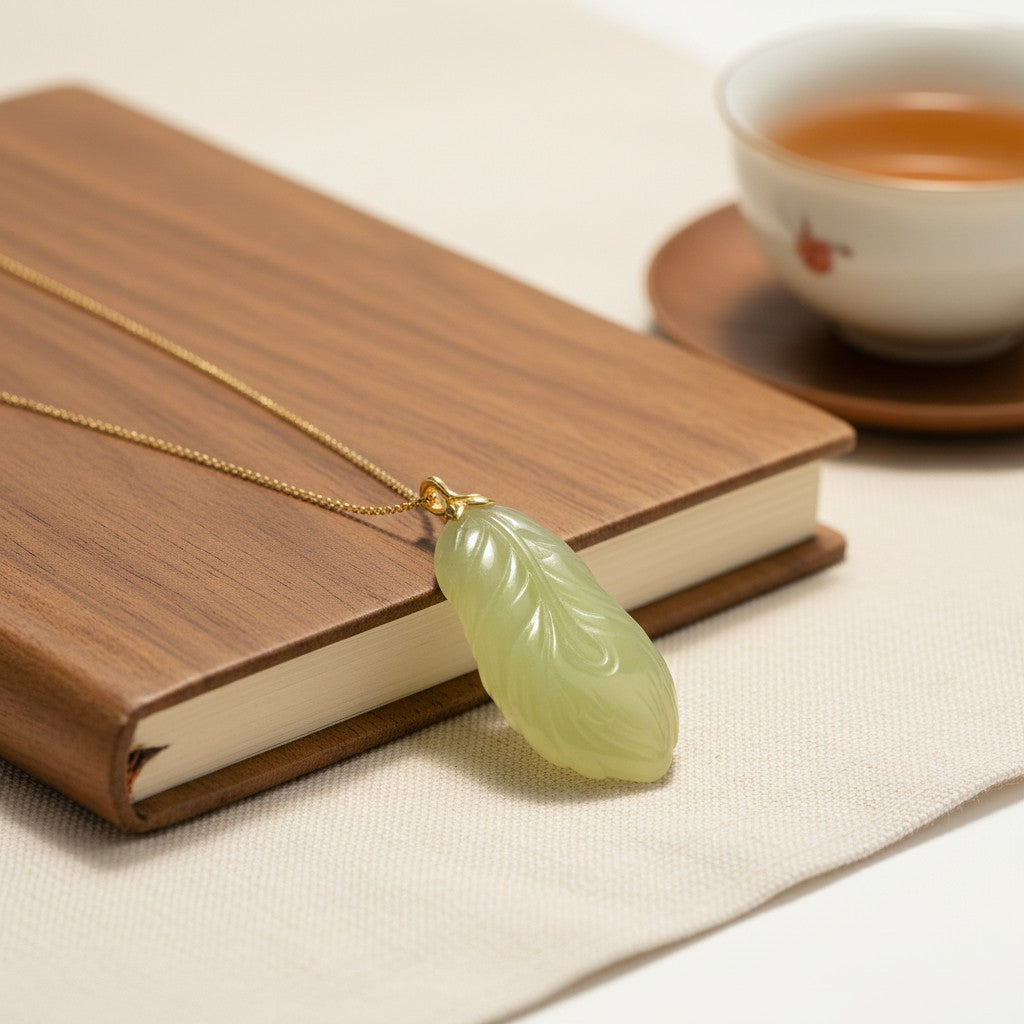 Sylvia Jewelry light green jade feather pendant necklace with a gold chain resting on a wooden notebook