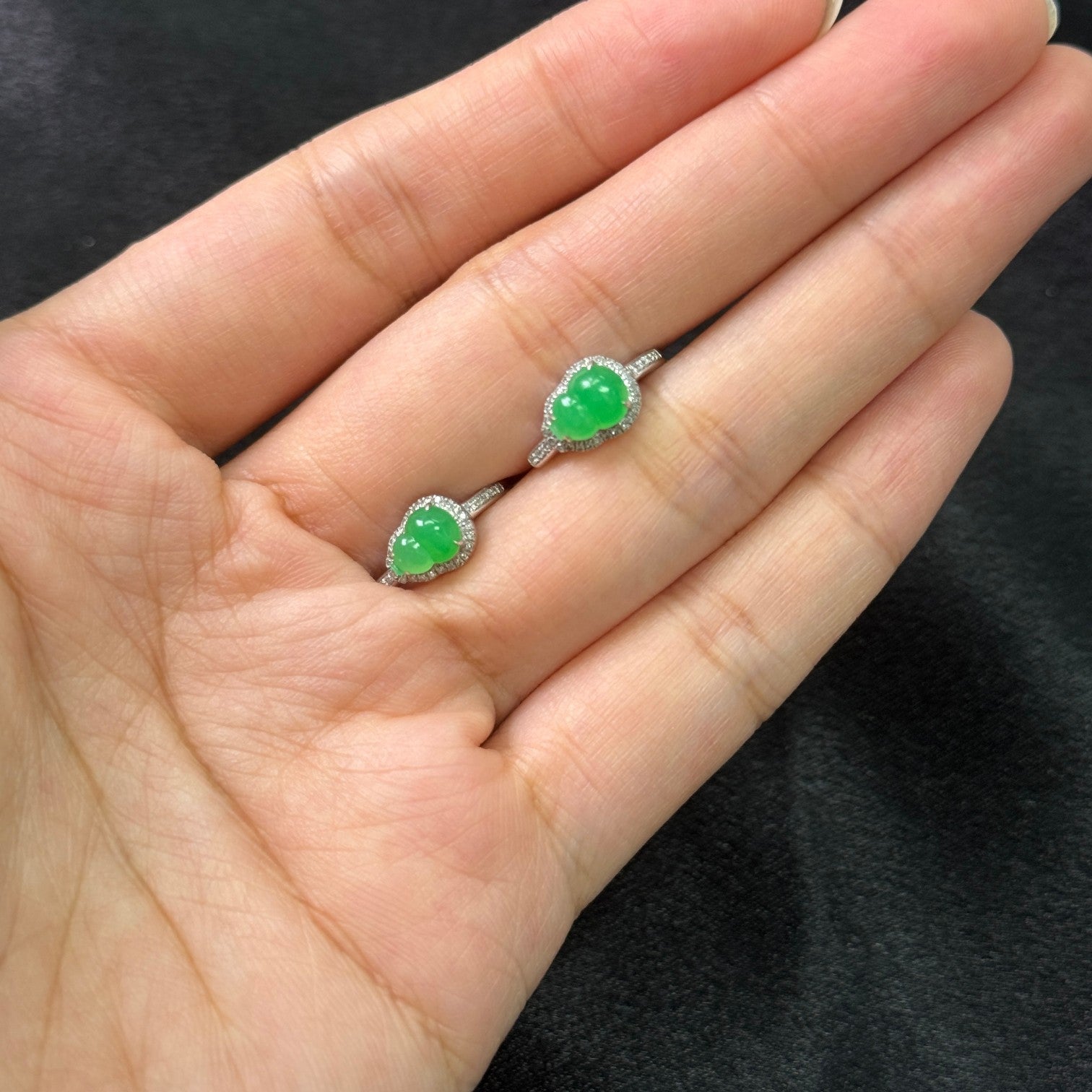 Sylvia Jewelry apple green jadeite Hulu huggie earrings in 18k white gold with diamond accents held in a palm.