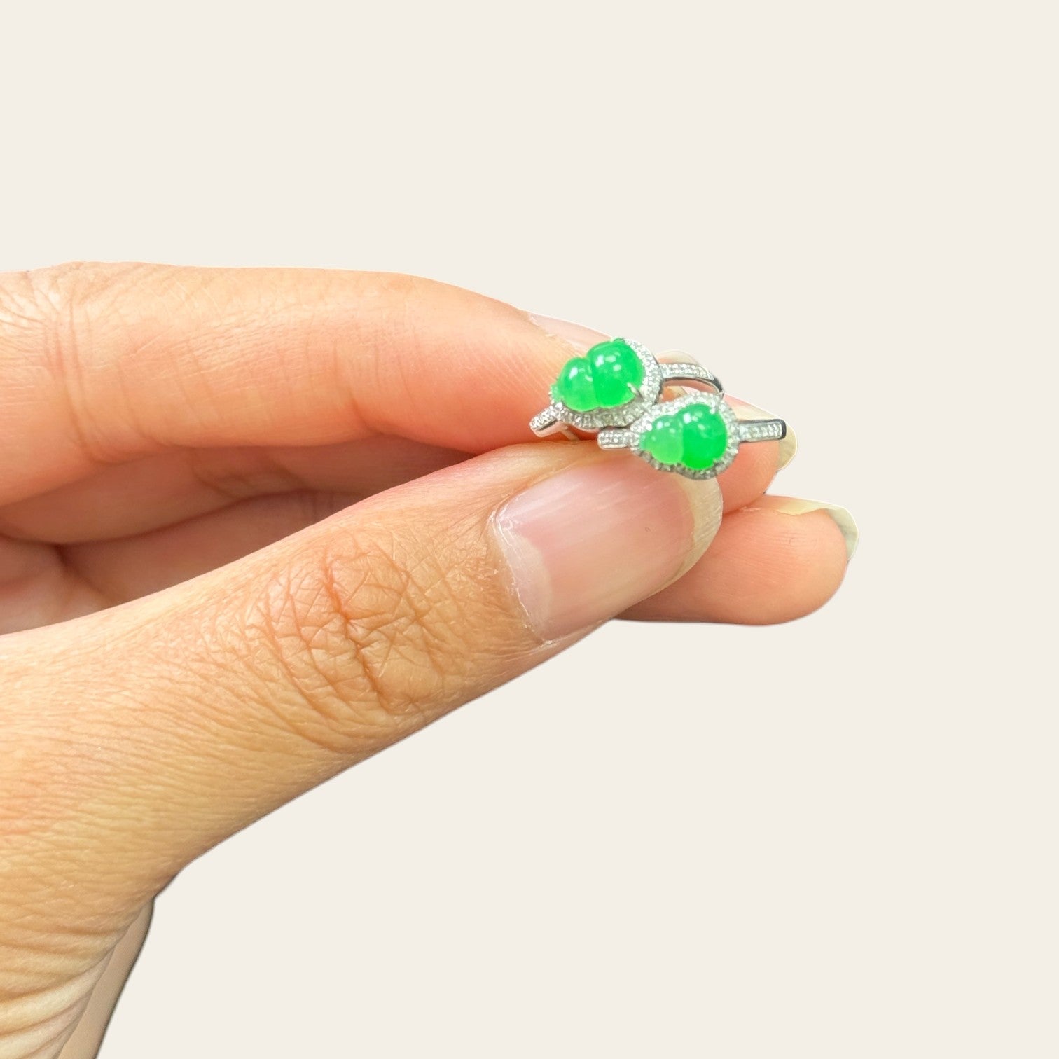 Sylvia Jewelry apple green jadeite Hulu huggie earrings in 18k white gold with diamond accents held in fingers.