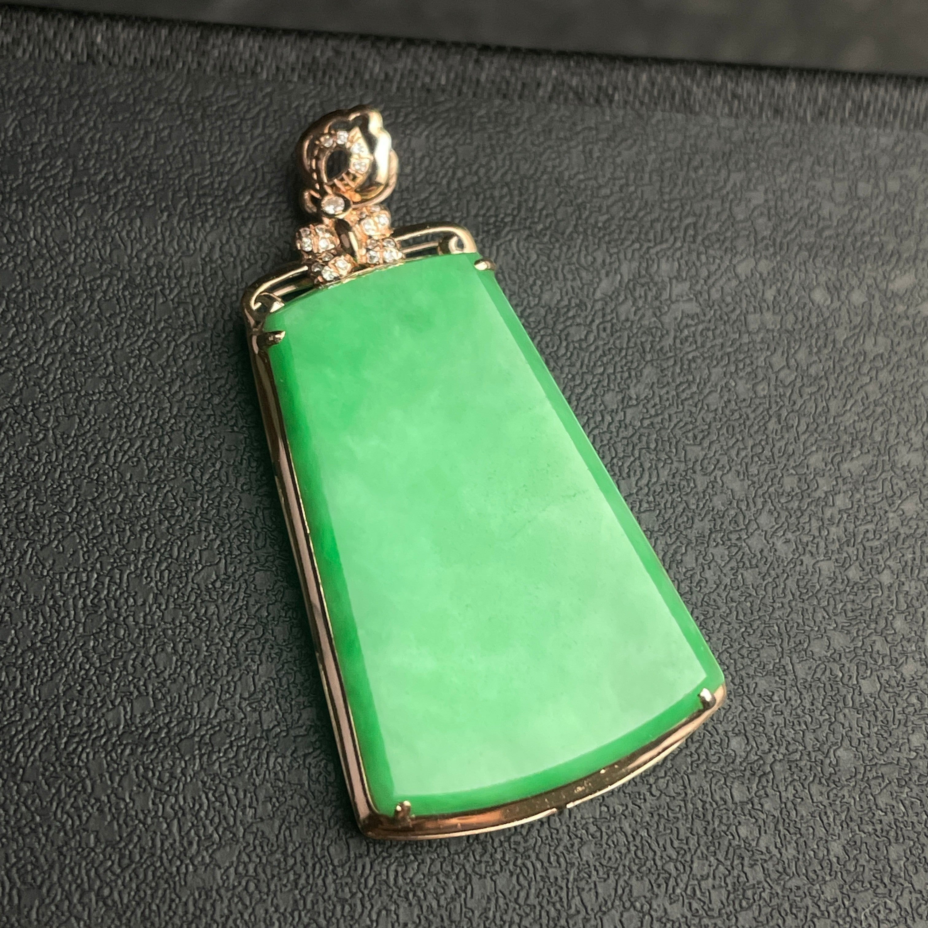 Sylvia Jewelry apple green jadeite trapezoid pendant with 18k gold and diamond bail on a dark textured background.