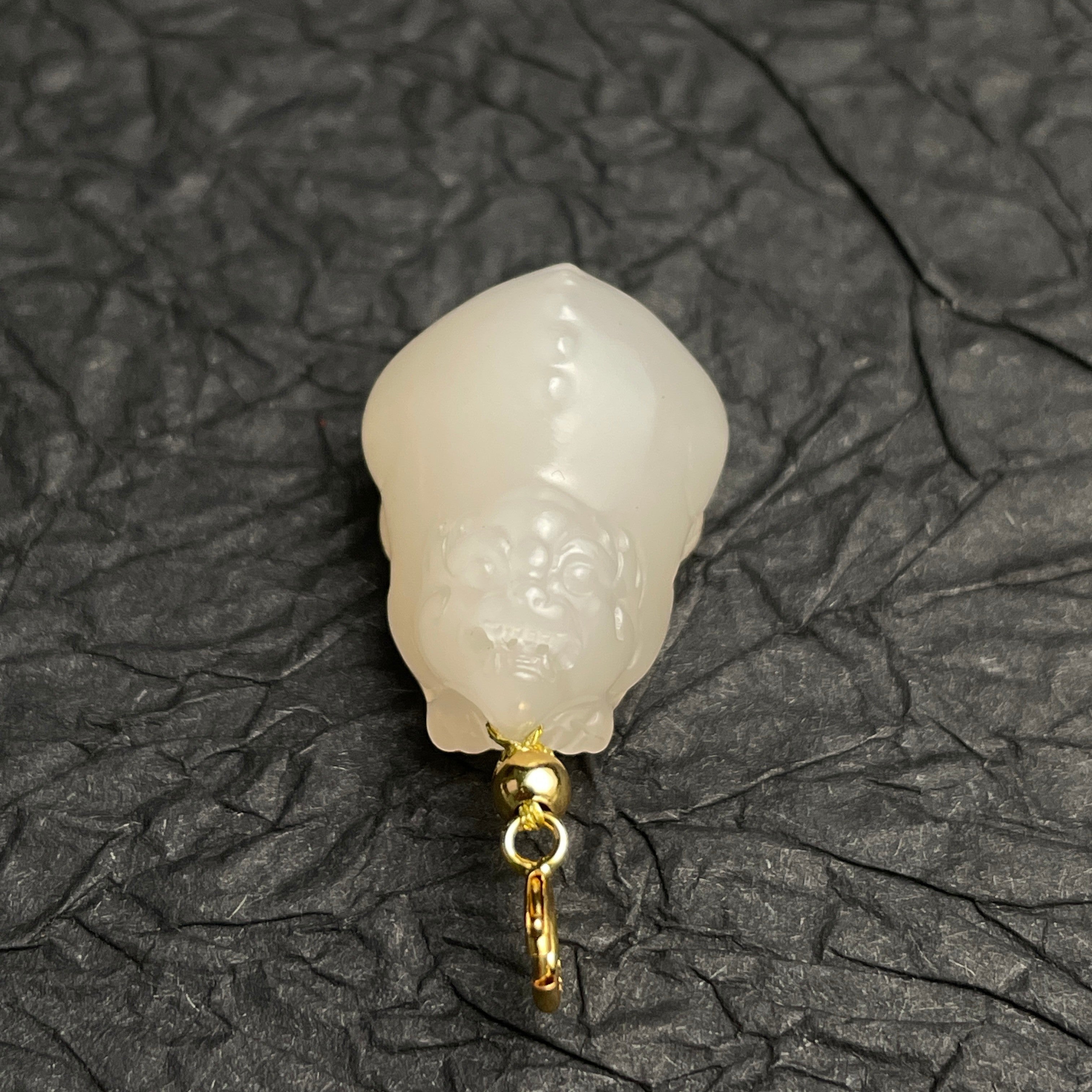 Sylvia Jewelry lotus-root pink Hetian nephrite jade PiXiu charm with a polished gold clasp on a dark textured background.