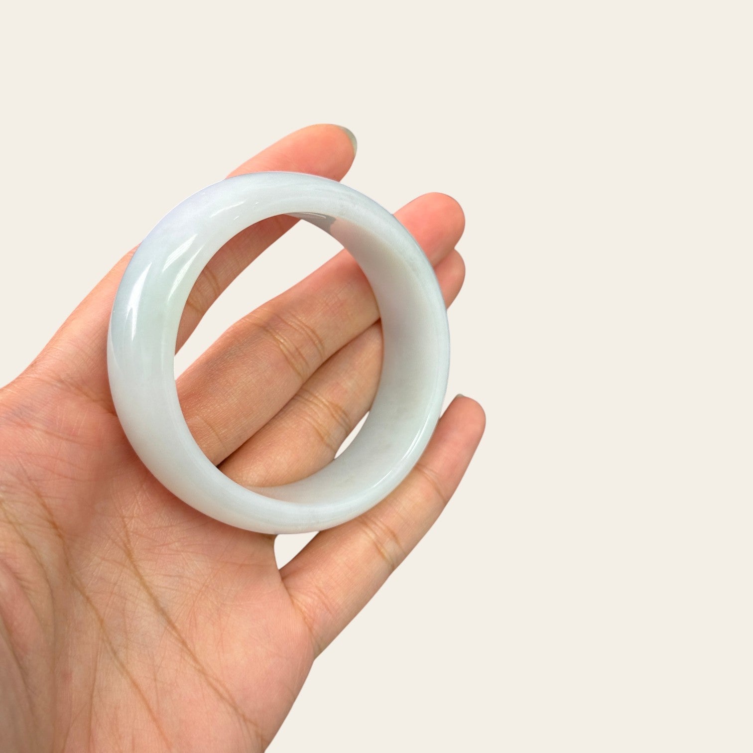Sylvia Jewelry ice-species white jadeite bangle with translucent, milky-clear finish held in a hand.