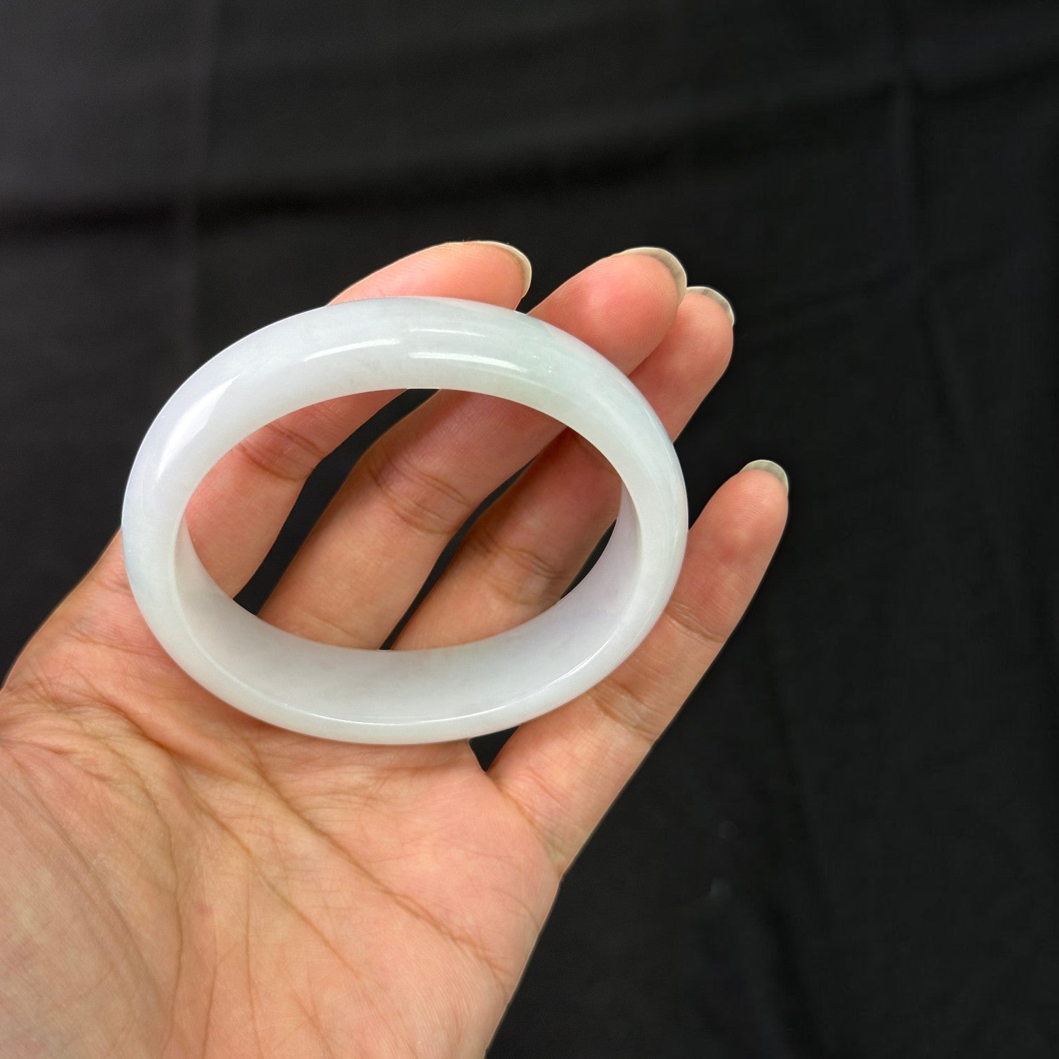 Sylvia Jewelry ice-species white jadeite bangle with translucent finish held in a hand against a black background.