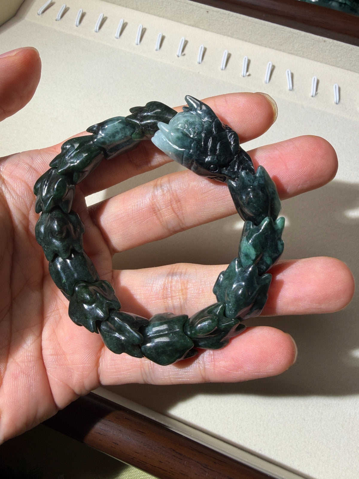 Deep green carved jadeite stretch bracelet held in hand, front view