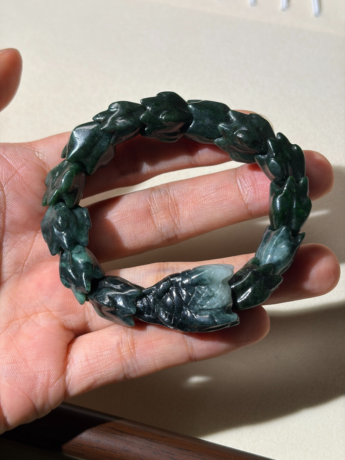 Deep green carved jadeite stretch bracelet held in hand, reverse view